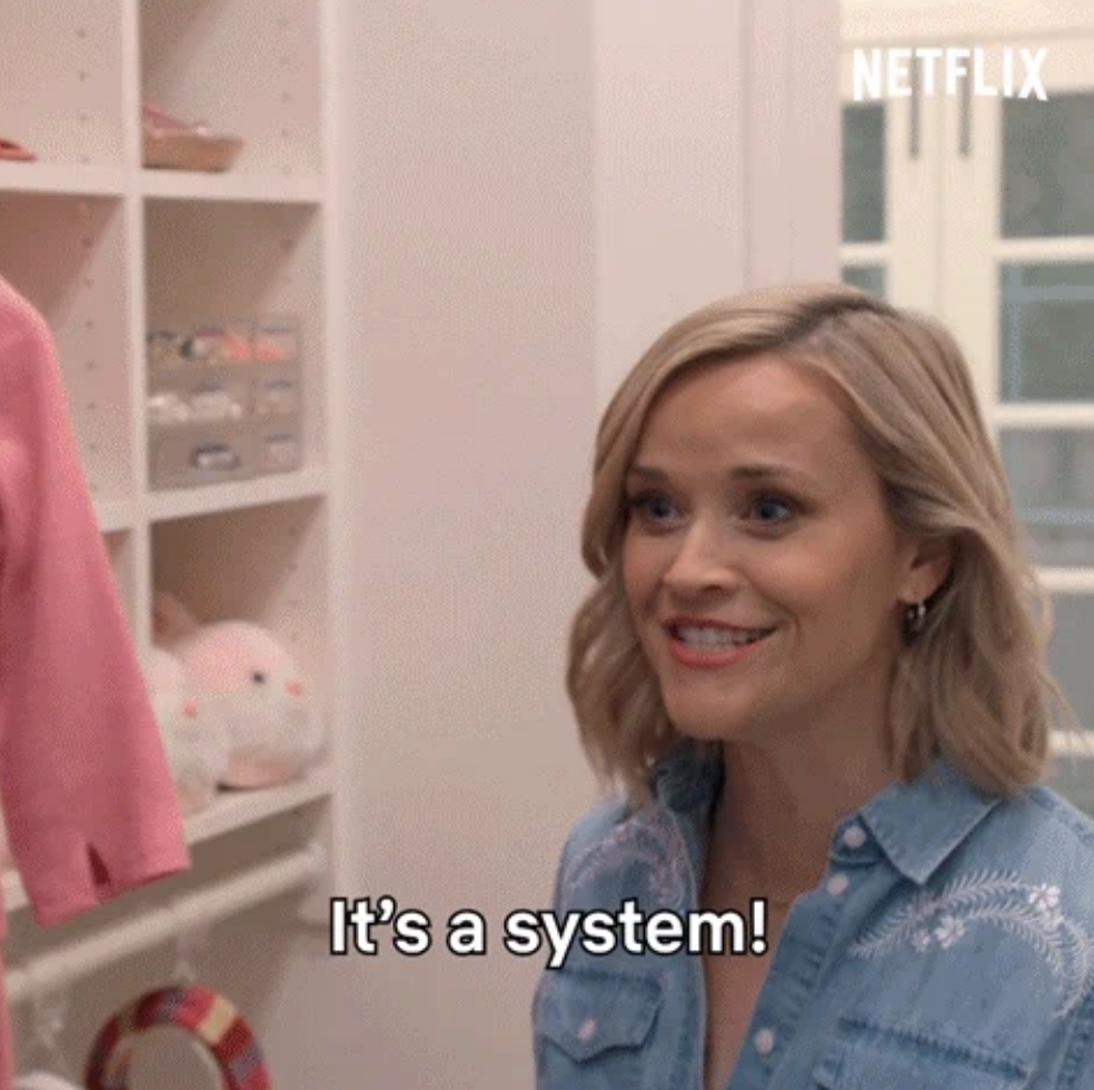 Reese Witherspoon smiles and speaks the caption, &quot;It&#x27;s a system!&quot;, in a home storage area.