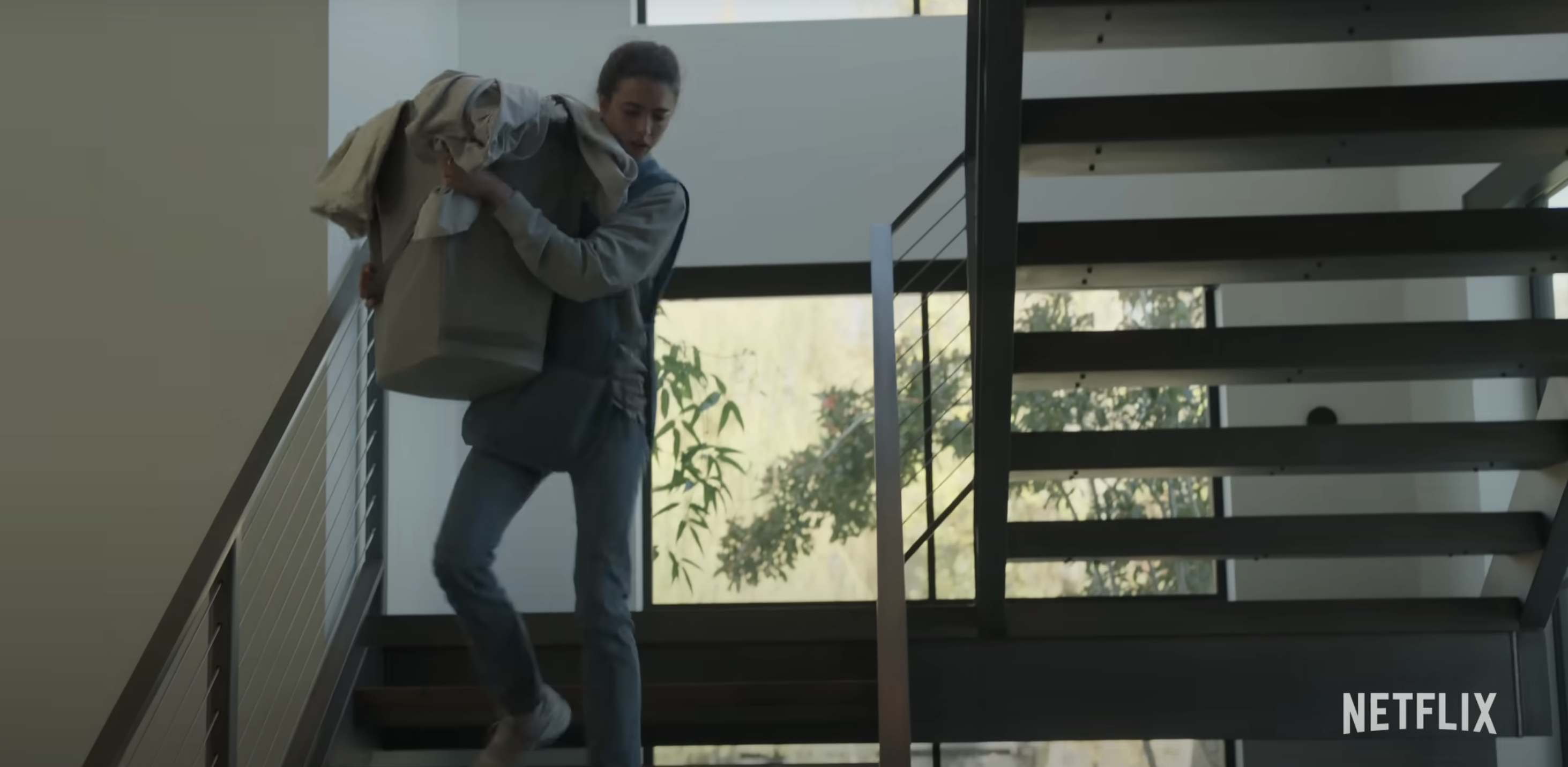 Alex from Maid carrying a large laundry basket down stairs in a modern home