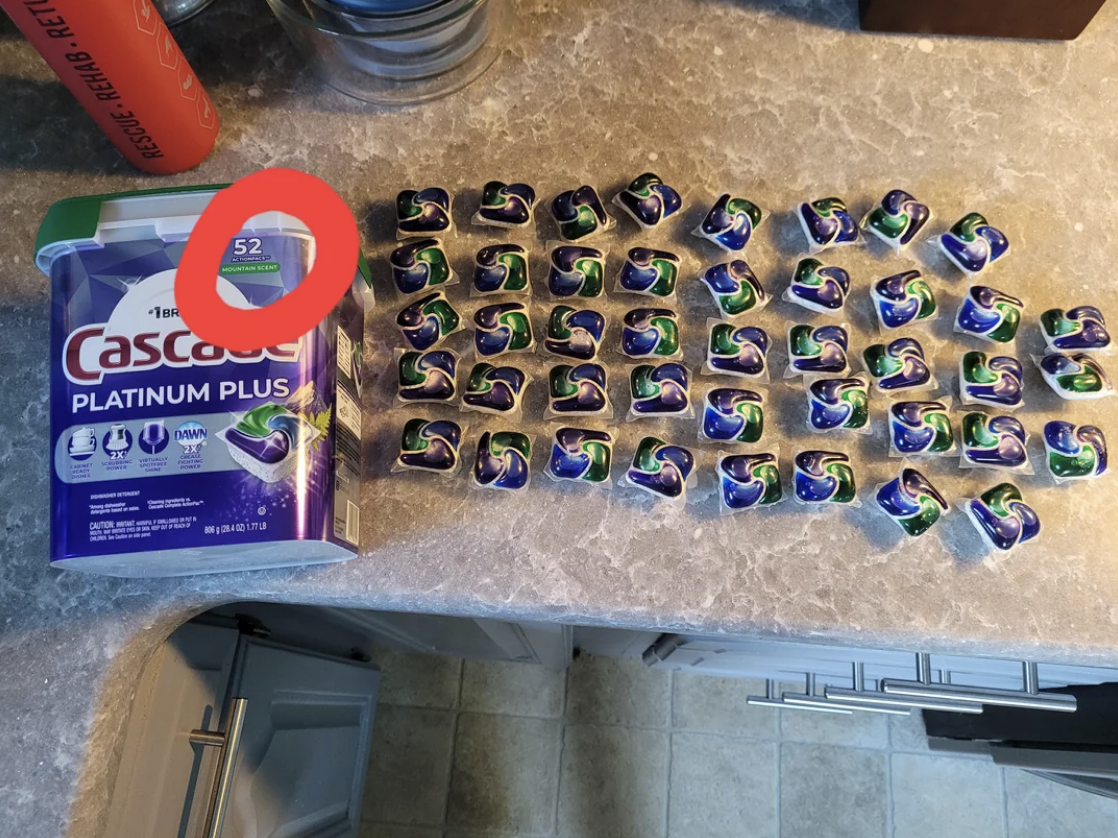 Cascade Platinum Plus dishwasher detergent pack container beside 52 individual packs neatly arranged on a kitchen counter
