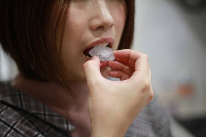 Close-up of a person eating ice, wearing a plaid shirt. The image focuses on the person&#x27;s mouth and hand