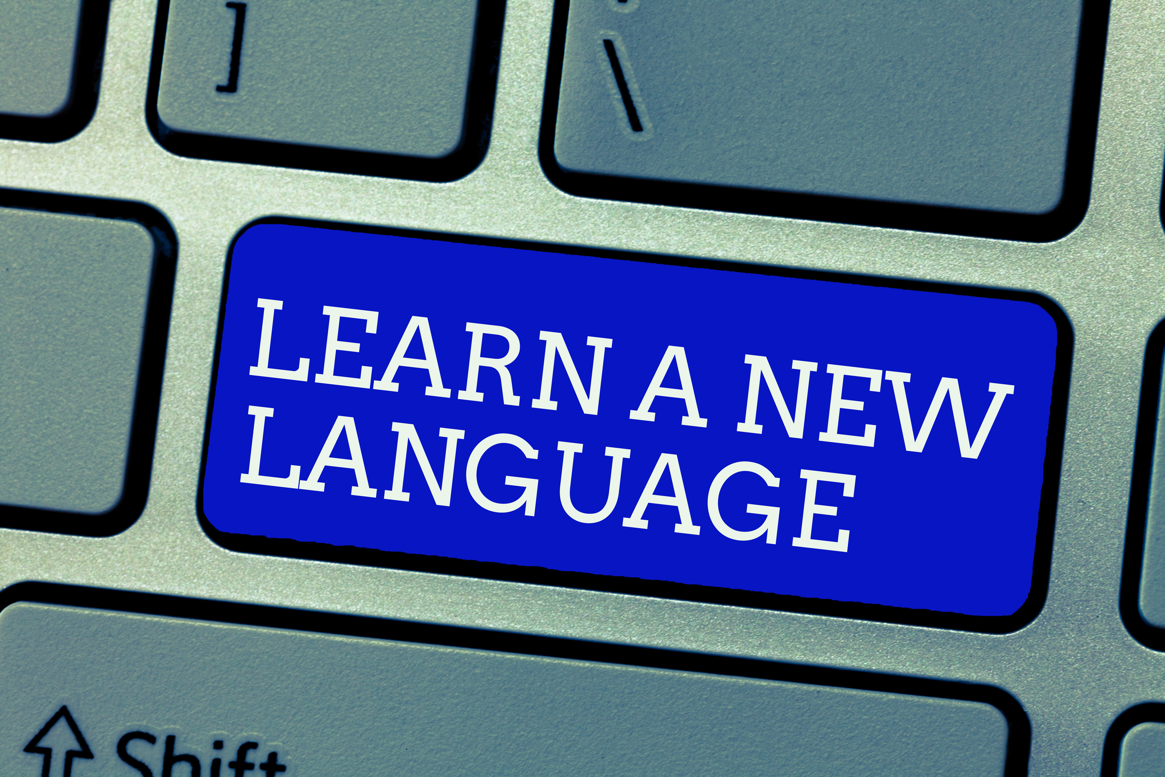 A keyboard with a blue key that reads &quot;LEARN A NEW LANGUAGE.&quot;