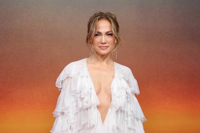 Jennifer Lopez posing on a red carpet wearing a deep v-neck, layered ruffle dress