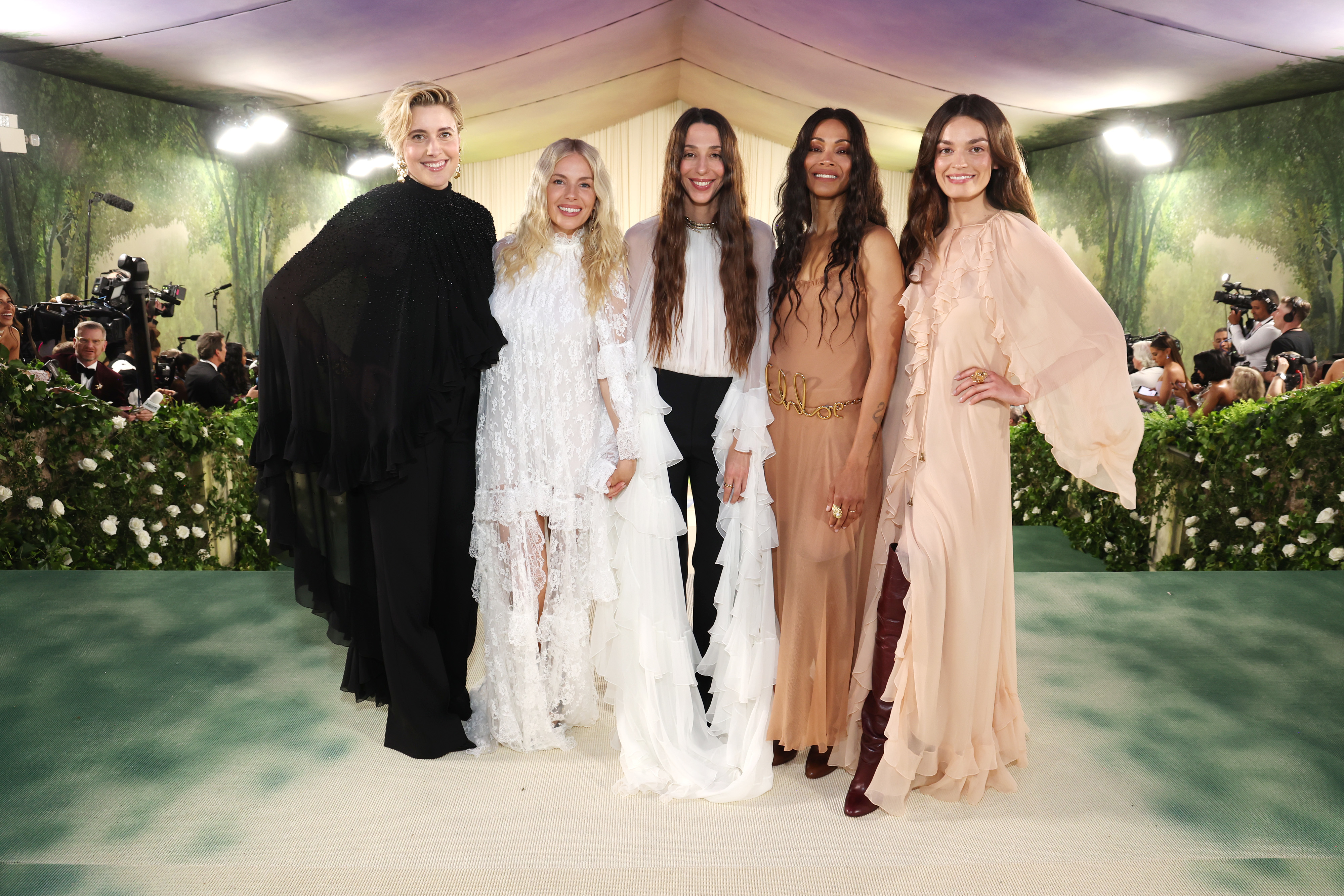 Five people standing together at an event, dressed in elegant outfits ranging from black to cream tones