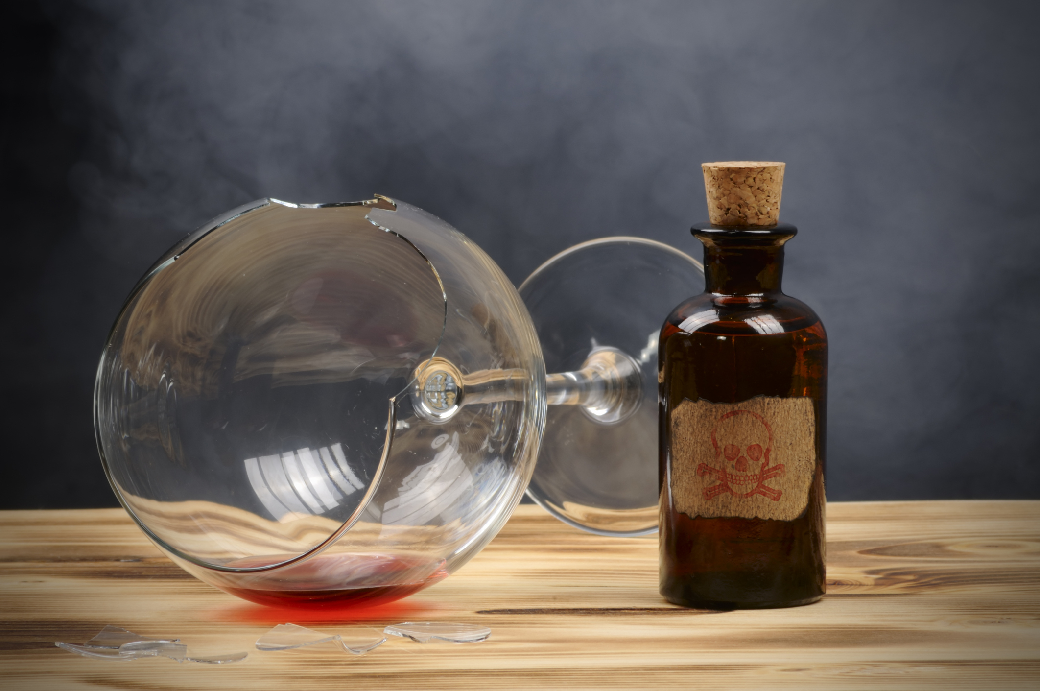 Empty wine glass tipped over with droplets and a sealed vintage bottle on a wooden surface