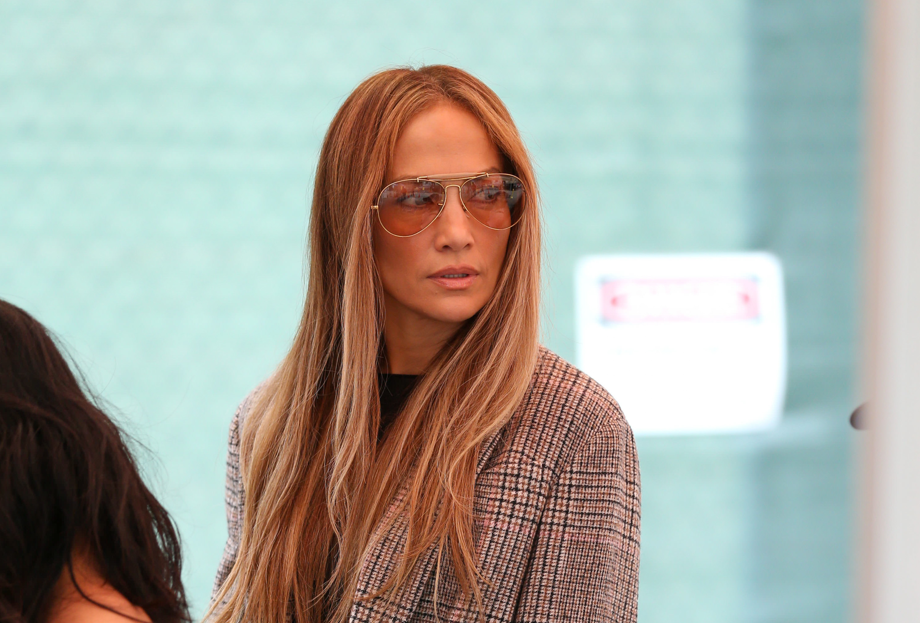 Jennifer Lopez wearing a stylish blazer and aviator sunglasses, looking to the side at an outdoor event