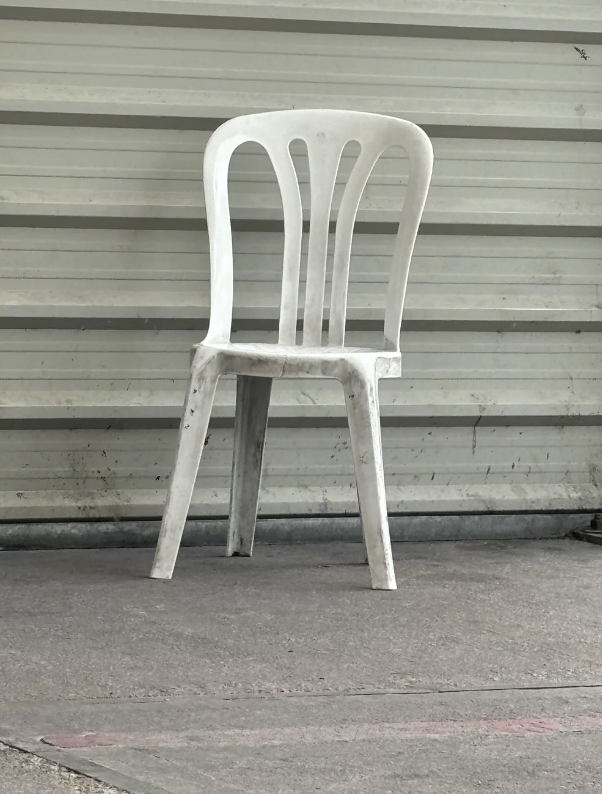 White plastic chair in front of a corrugated metal wall, placed on a concrete floor