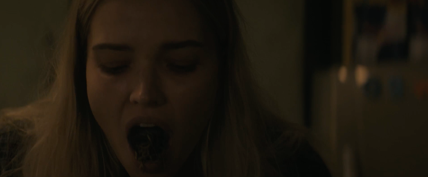 Close-up of a person with long hair eating food in a dimly lit room