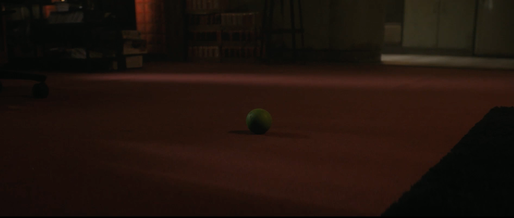 A lone green ball rests on a carpet in a dimly lit room