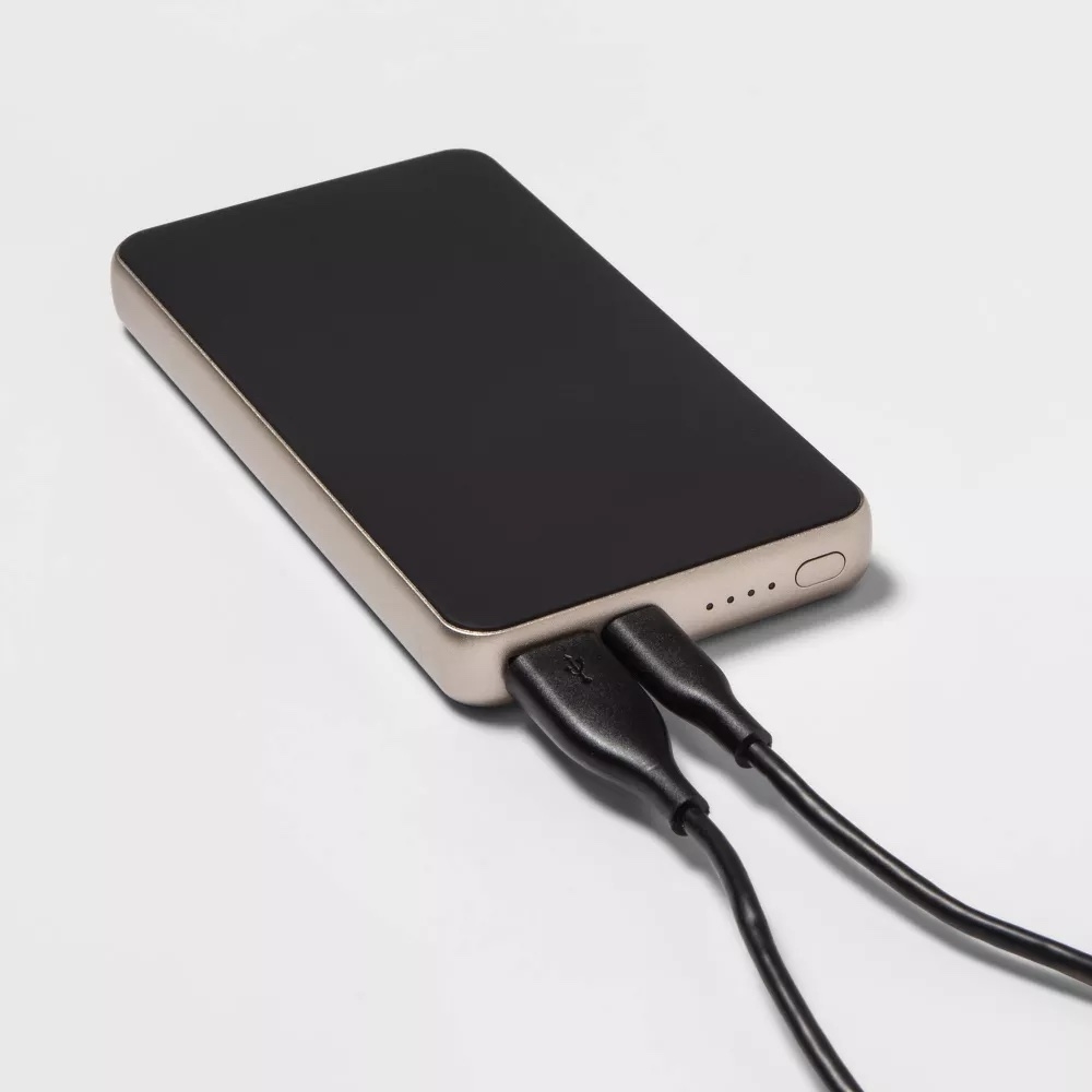 A sleek portable power bank with two charging cables plugged in, shown against a plain background