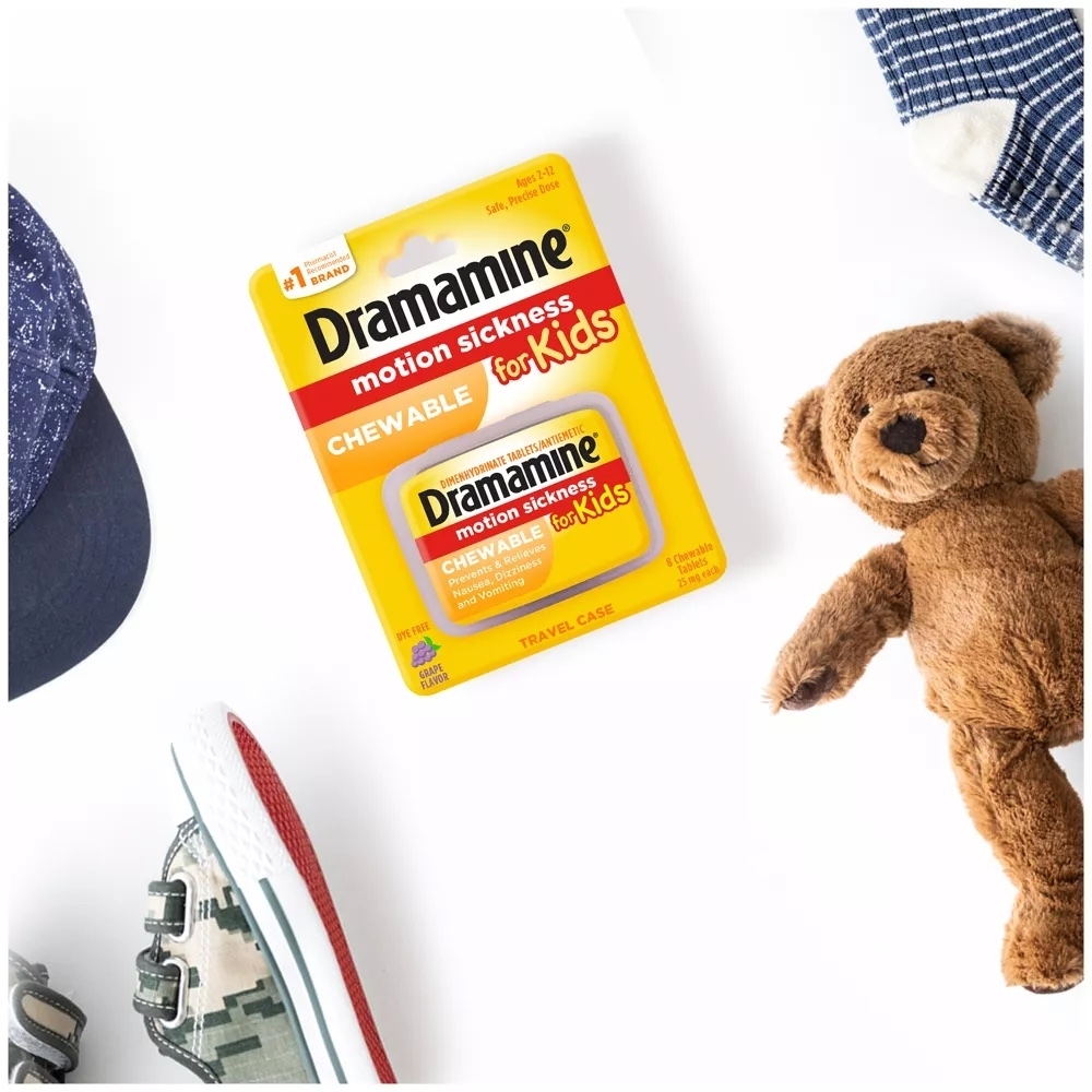 Dramamine Kids Chewable Motion Sickness Relief package next to a teddy bear, shoe, and hat, highlighting travel essentials for children