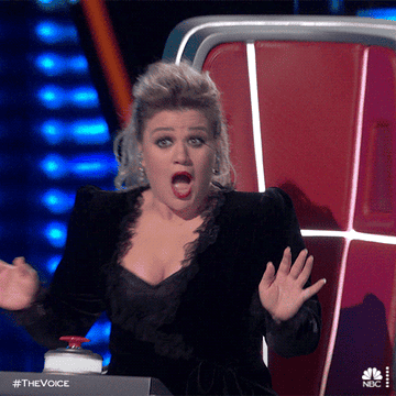 Kelly Clarkson on The Voice, expressing surprise with her mouth open and hands up, seated at her judge&#x27;s chair