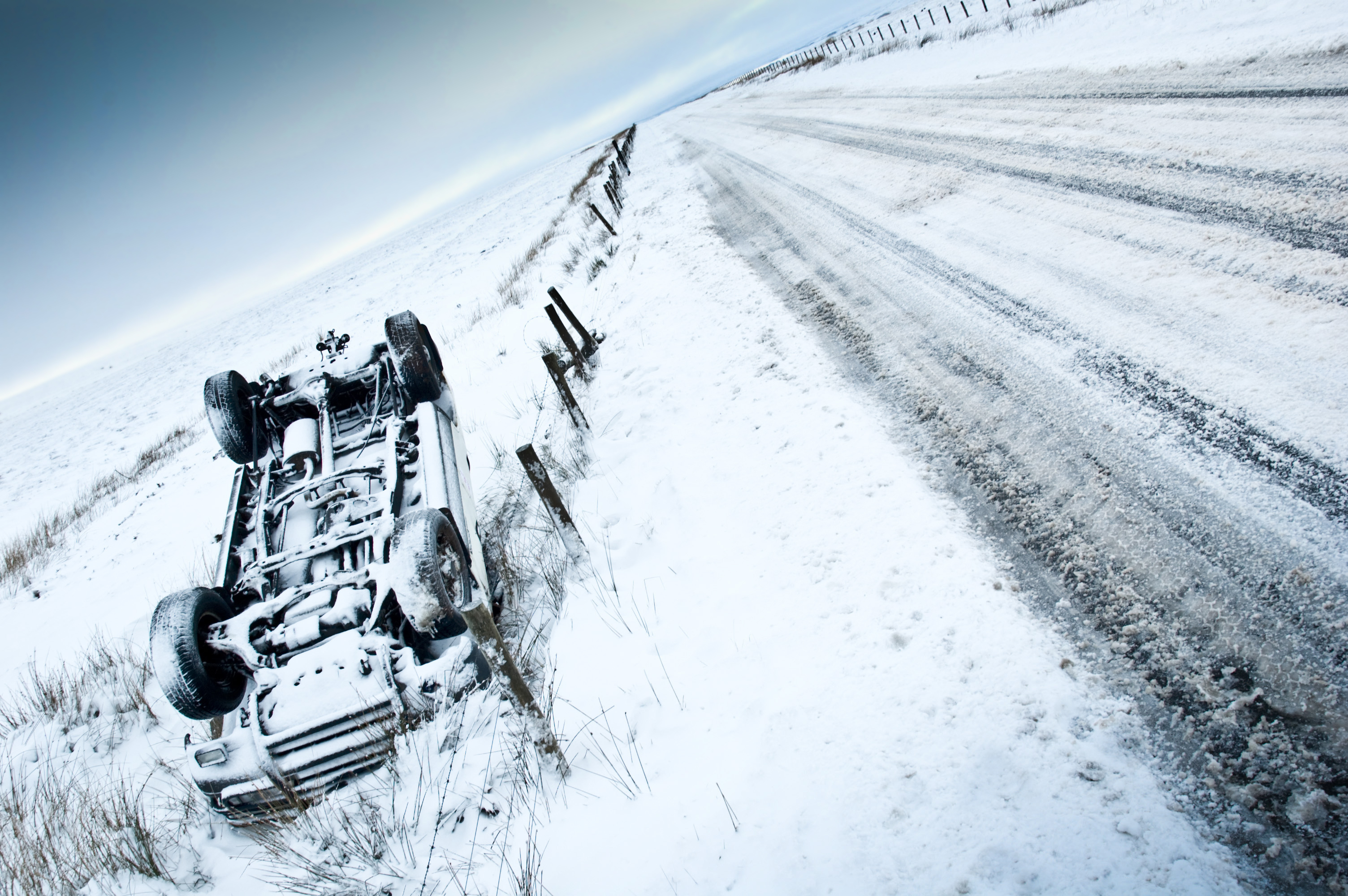 An overturned car lies upside down beside a snowy, deserted road, indicating an accident in a wintery landscape