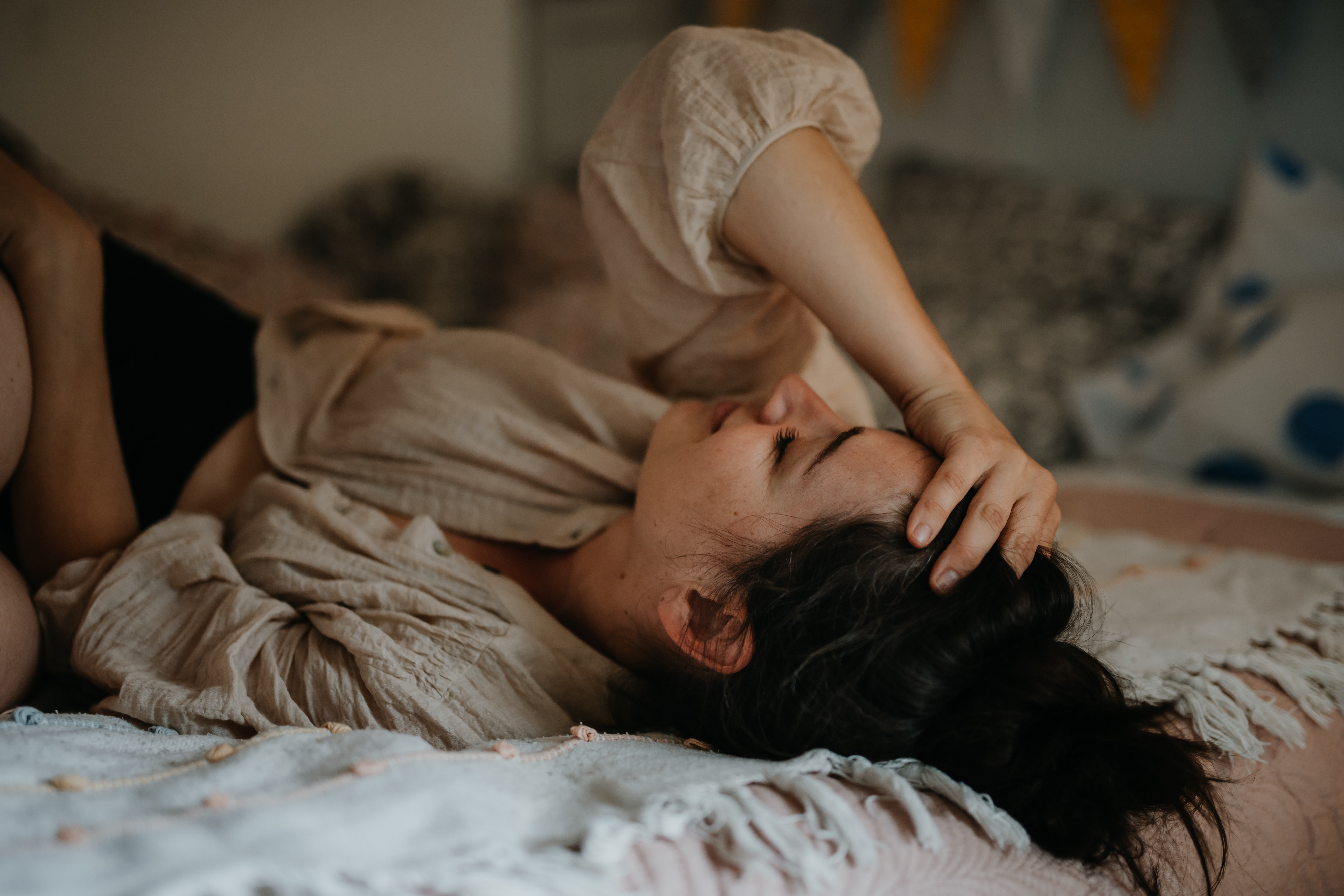 A woman is lying on her back on a bed, with her hand resting on her forehead, looking relaxed and thoughtful