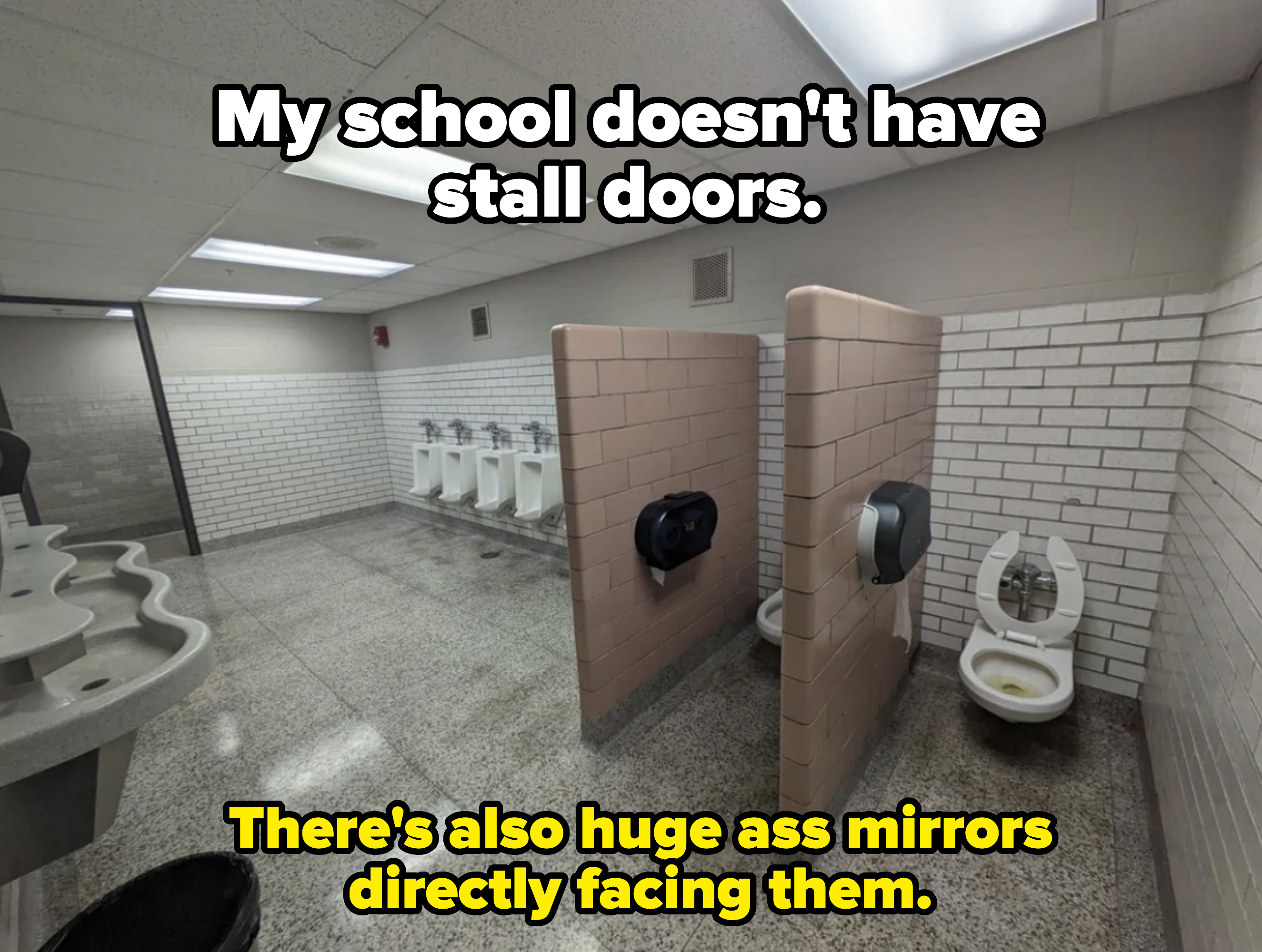 An empty men&#x27;s restroom with urinals on the far wall, two stalls, and a multi-sink area. The stall toilets have open lids, and there are light fixtures on the ceiling