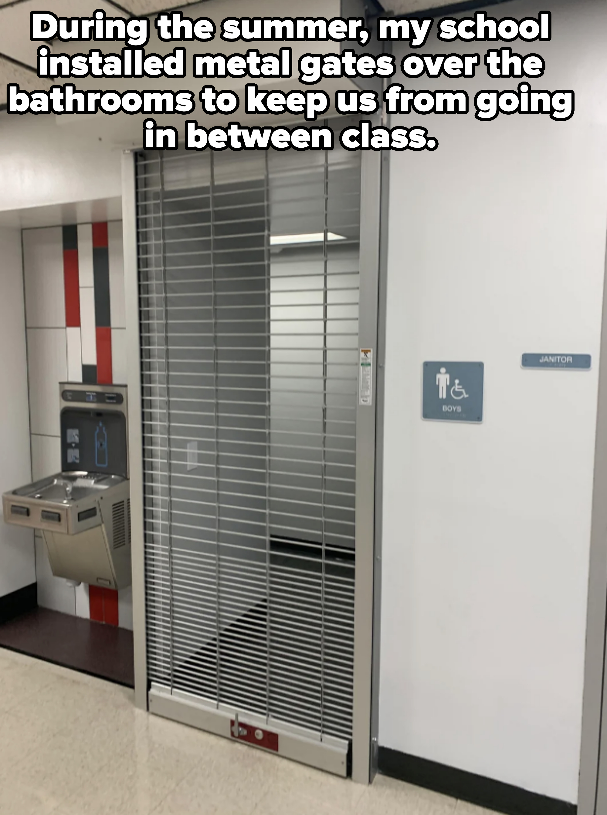 A closed security gate covers an entrance. To the left, there is a drinking fountain, and to the right, a sign indicates an accessible boys&#x27; restroom next to a janitor&#x27;s closet