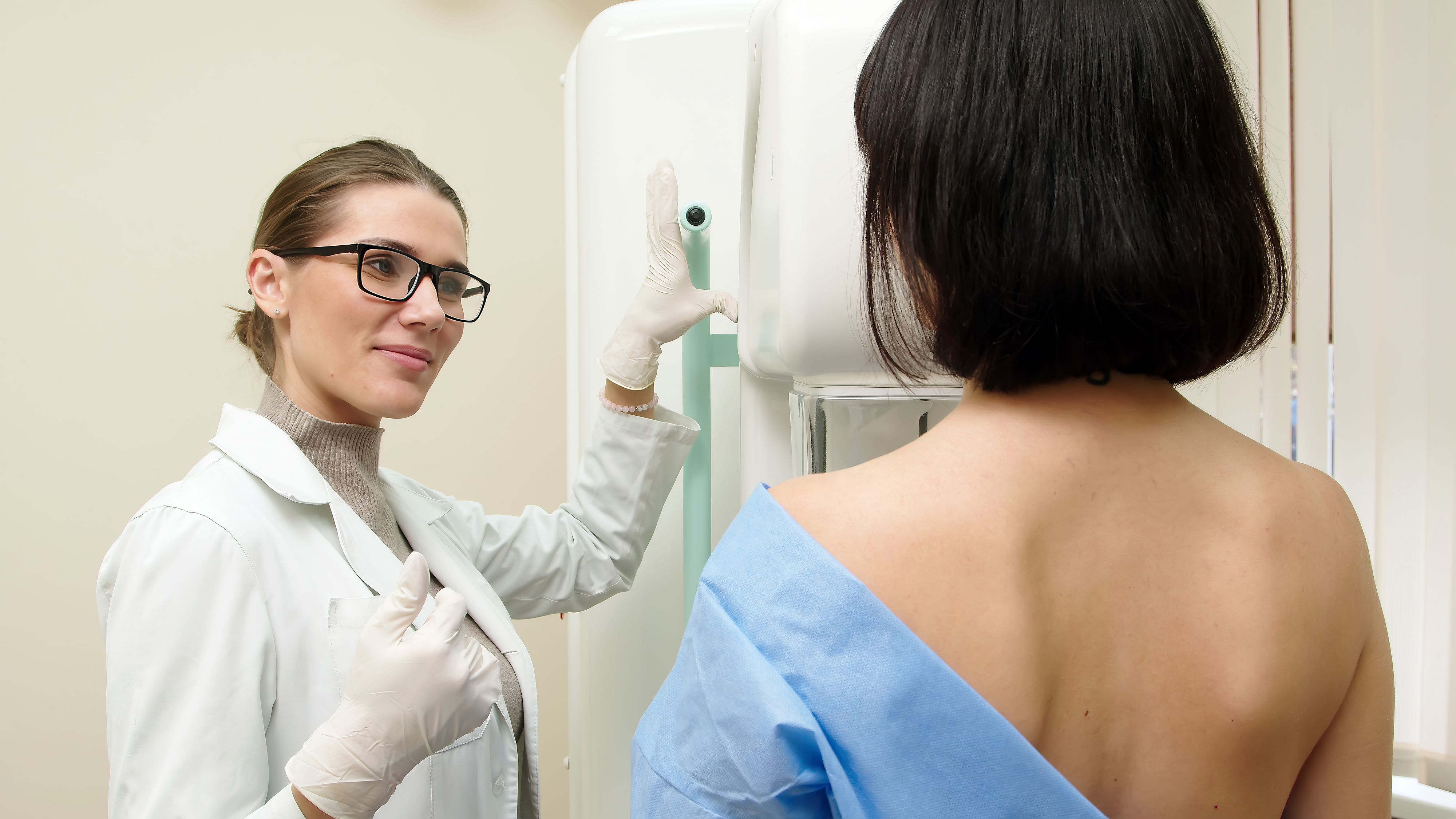 A healthcare professional gives a mammogram to a patient wearing a gown