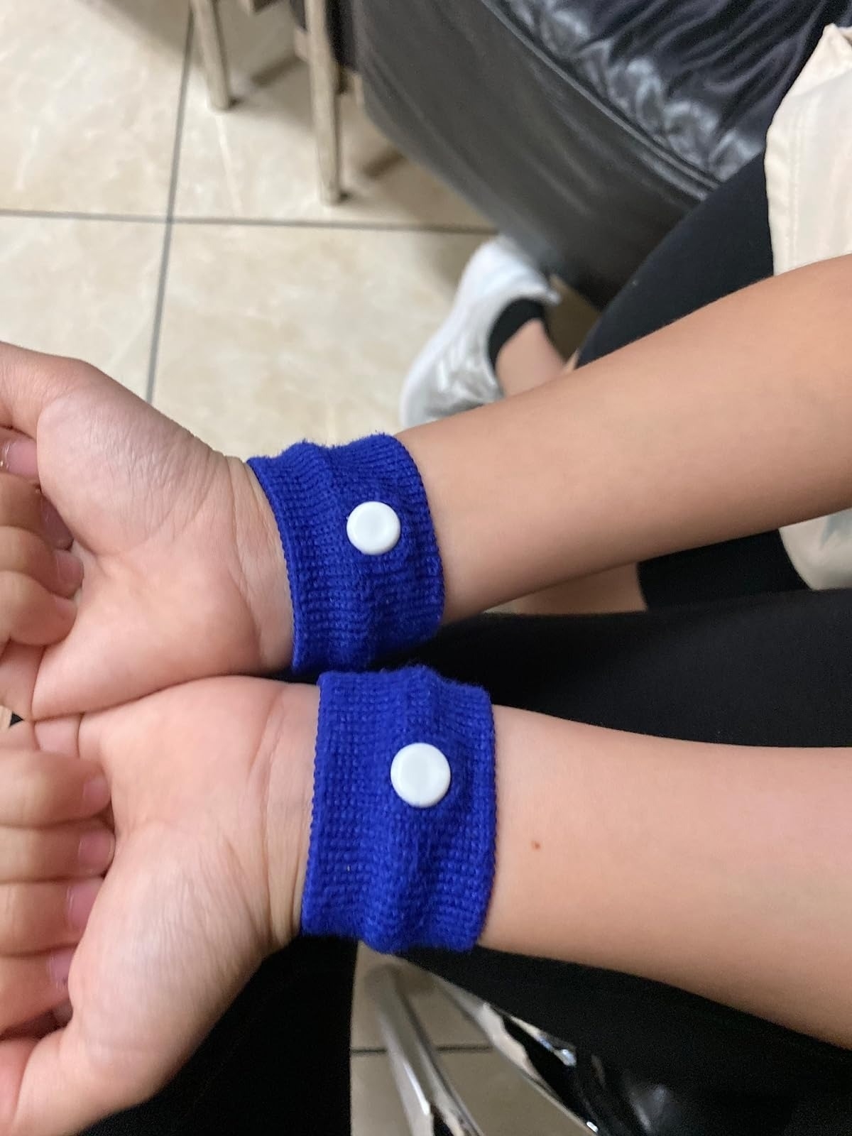 Close-up of wrists wearing blue wristbands with white buttons