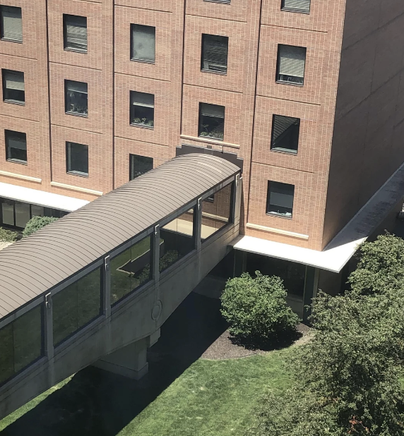 A brick building with a covered walkway connecting to an upper floor entrance. Green bushes surround the area. No people are visible