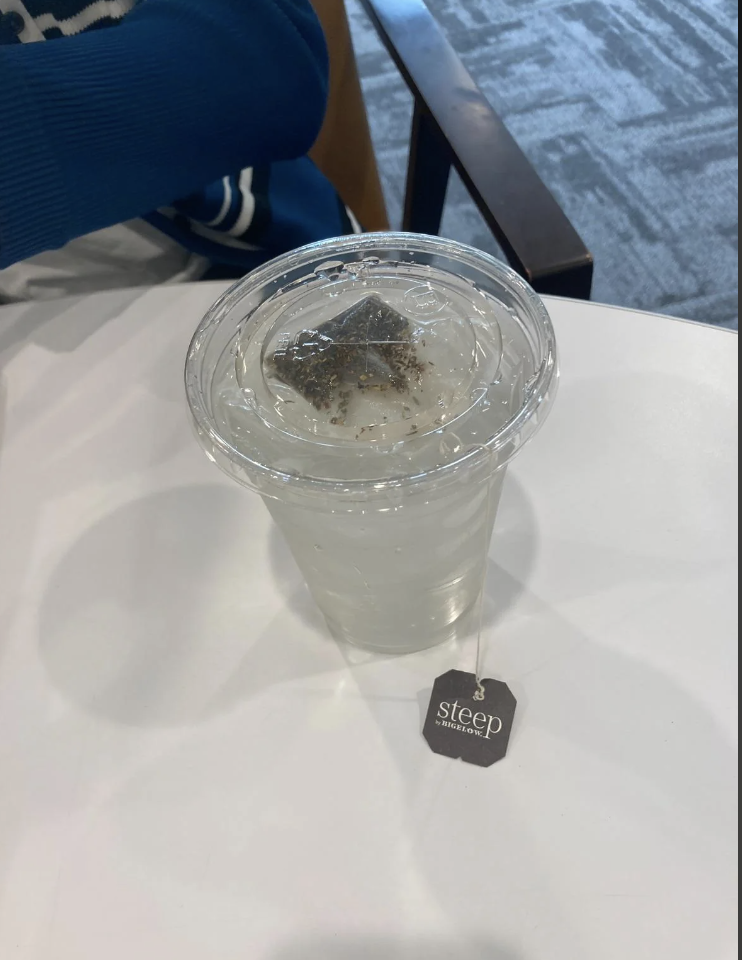 A clear plastic cup filled with iced water and a tea bag labeled &quot;steep&quot; on a table