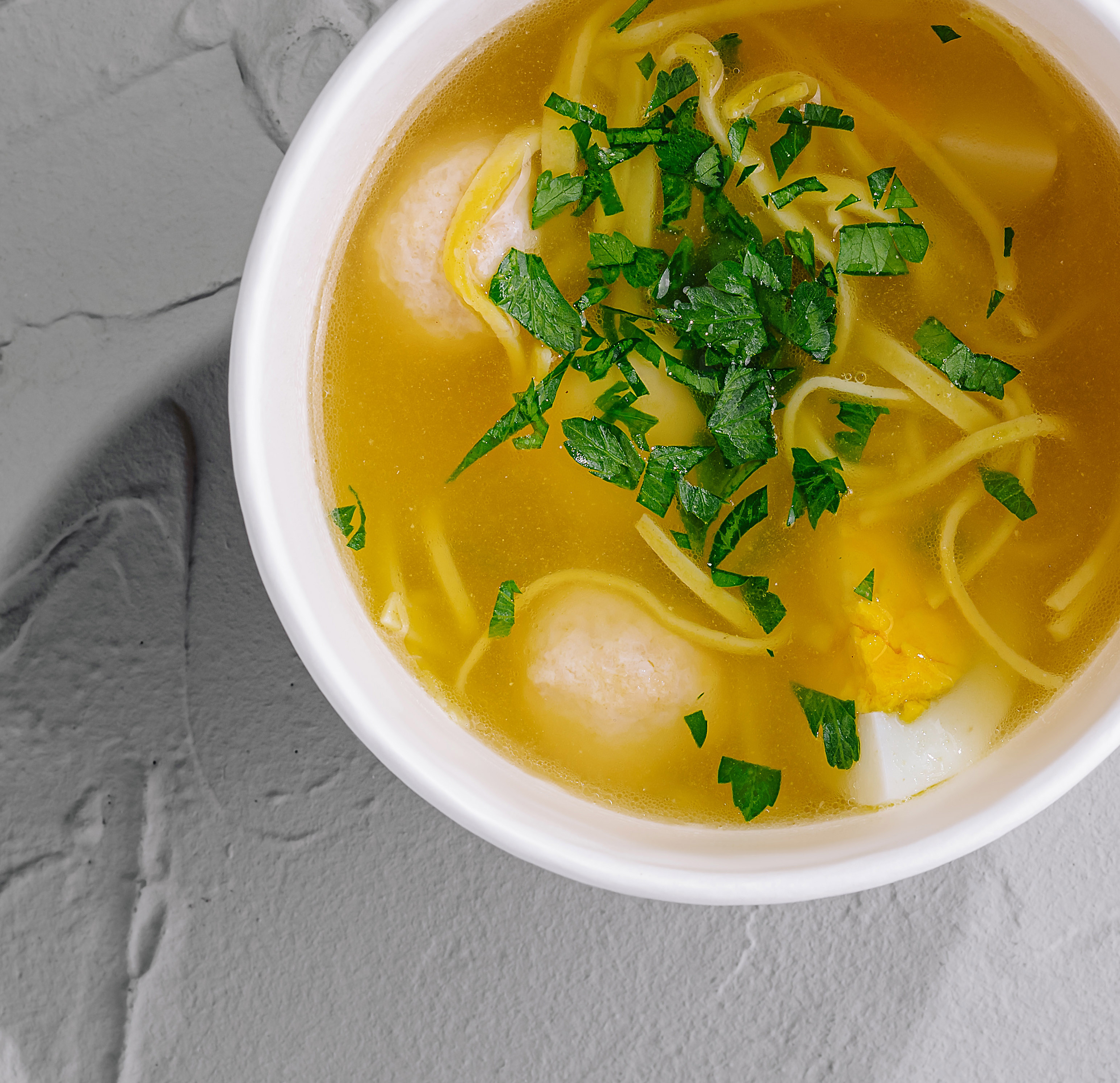 A bowl of soup with noodles, meatballs, and herbs garnished on top