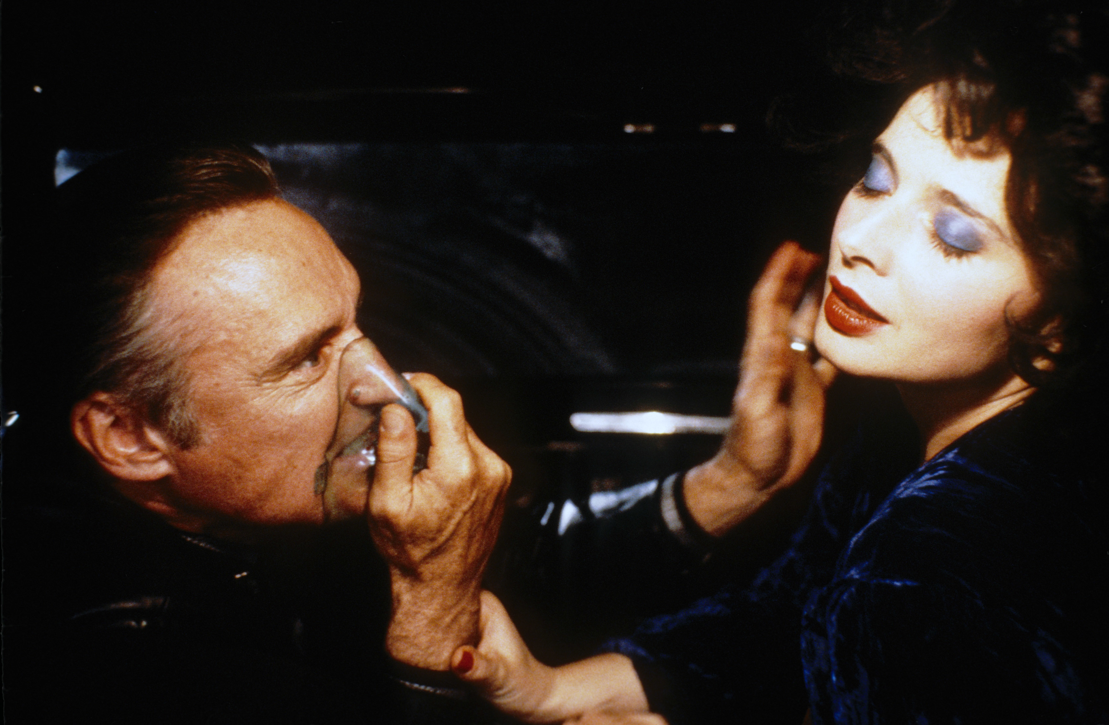 Dennis Hopper and Isabella Rossellini in an intense moment from a scene in a movie. Dennis holds his hand on his face; Isabella is reaching out, showing distress