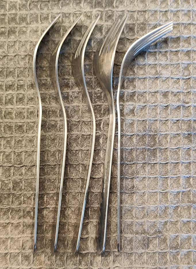 Four bent forks with twisted prongs placed side by side on a textured surface