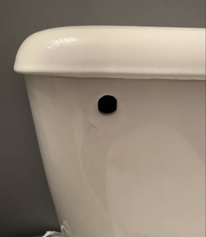 Close-up image of a white toilet tank with a small, round hole on the side