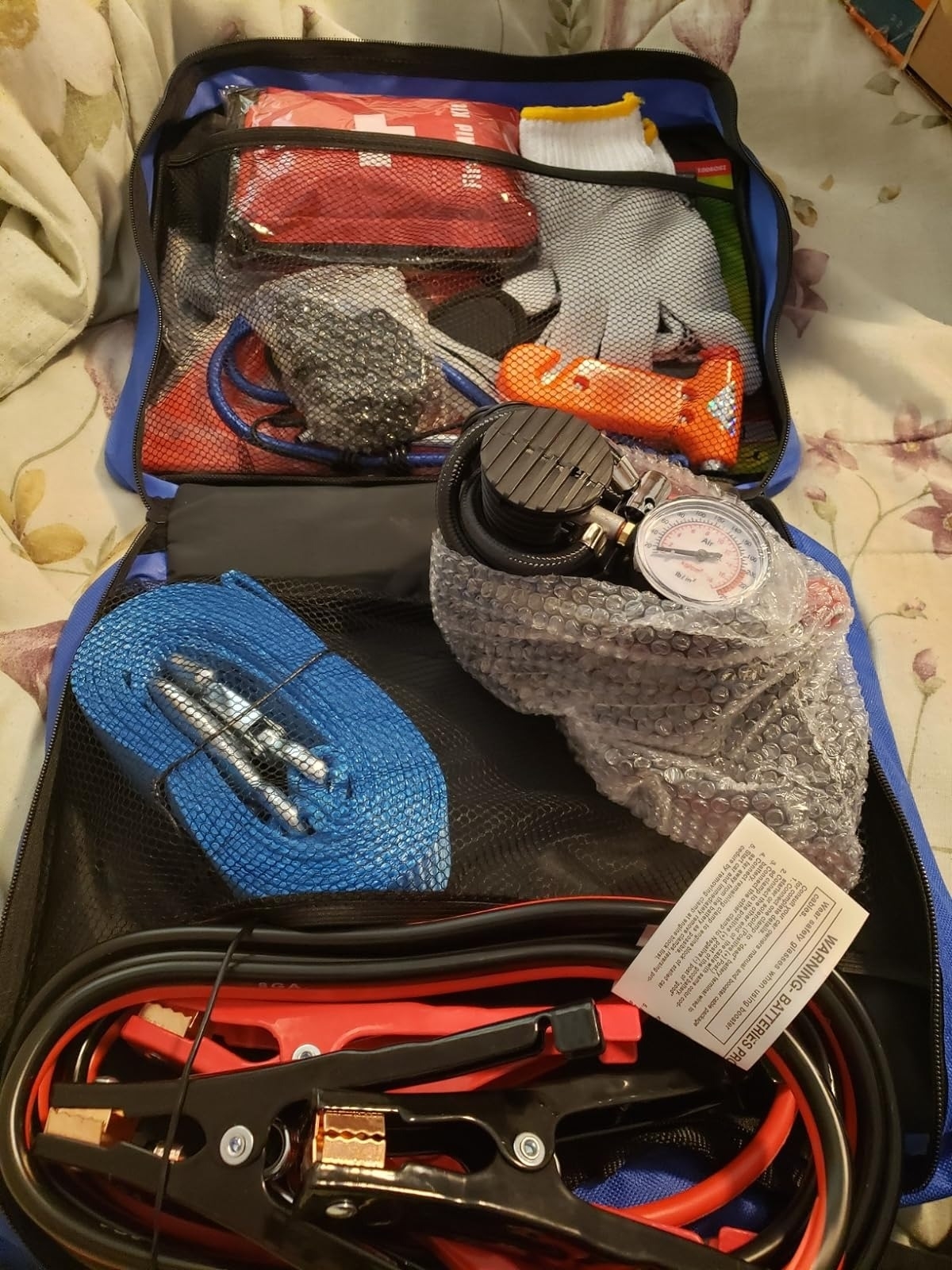 Open emergency car kit with gloves, jump cables, tire pressure gauge, and first aid supplies