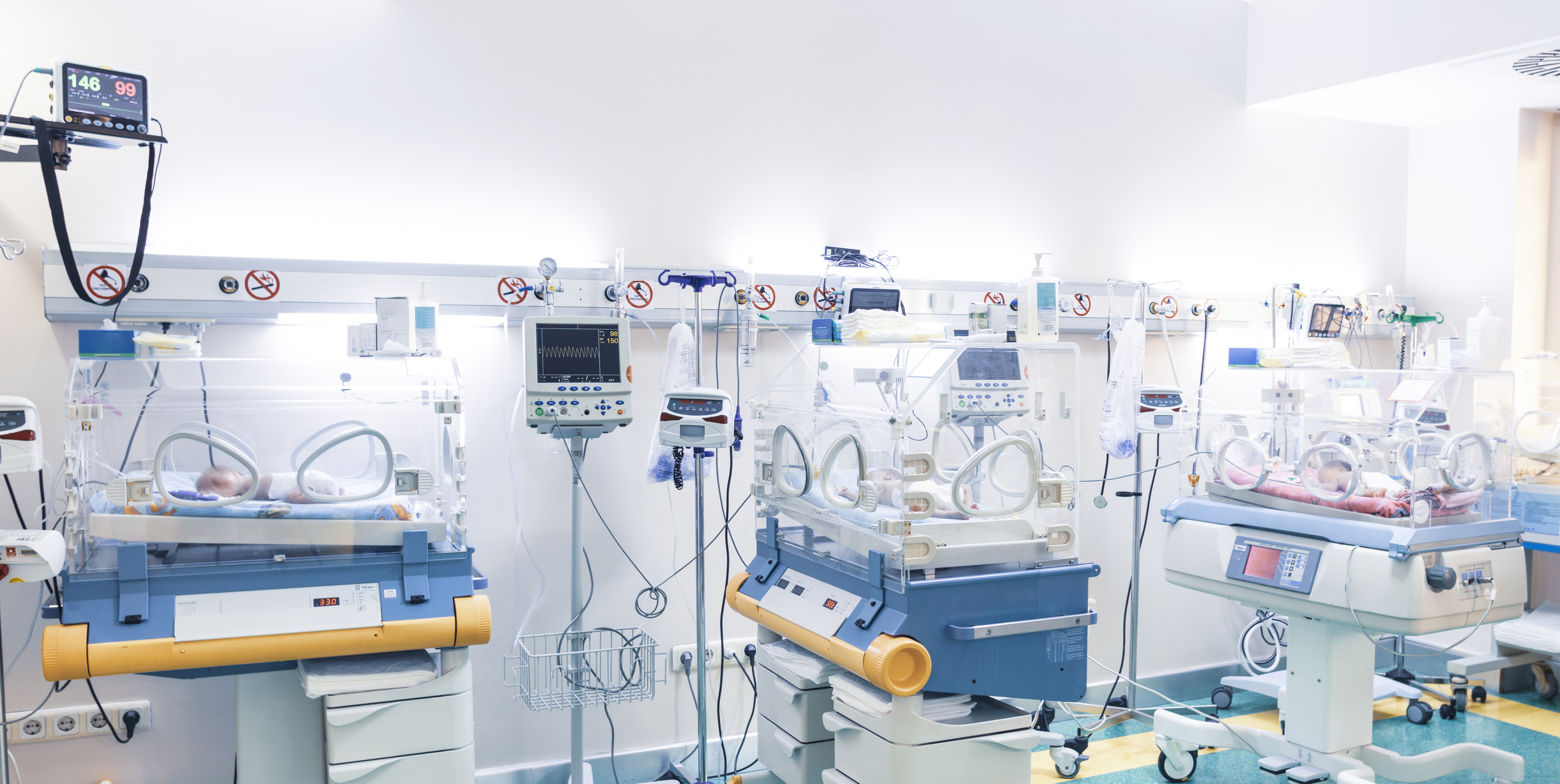 Newborn babies in incubators in a neonatal intensive care unit, surrounded by medical equipment and monitors