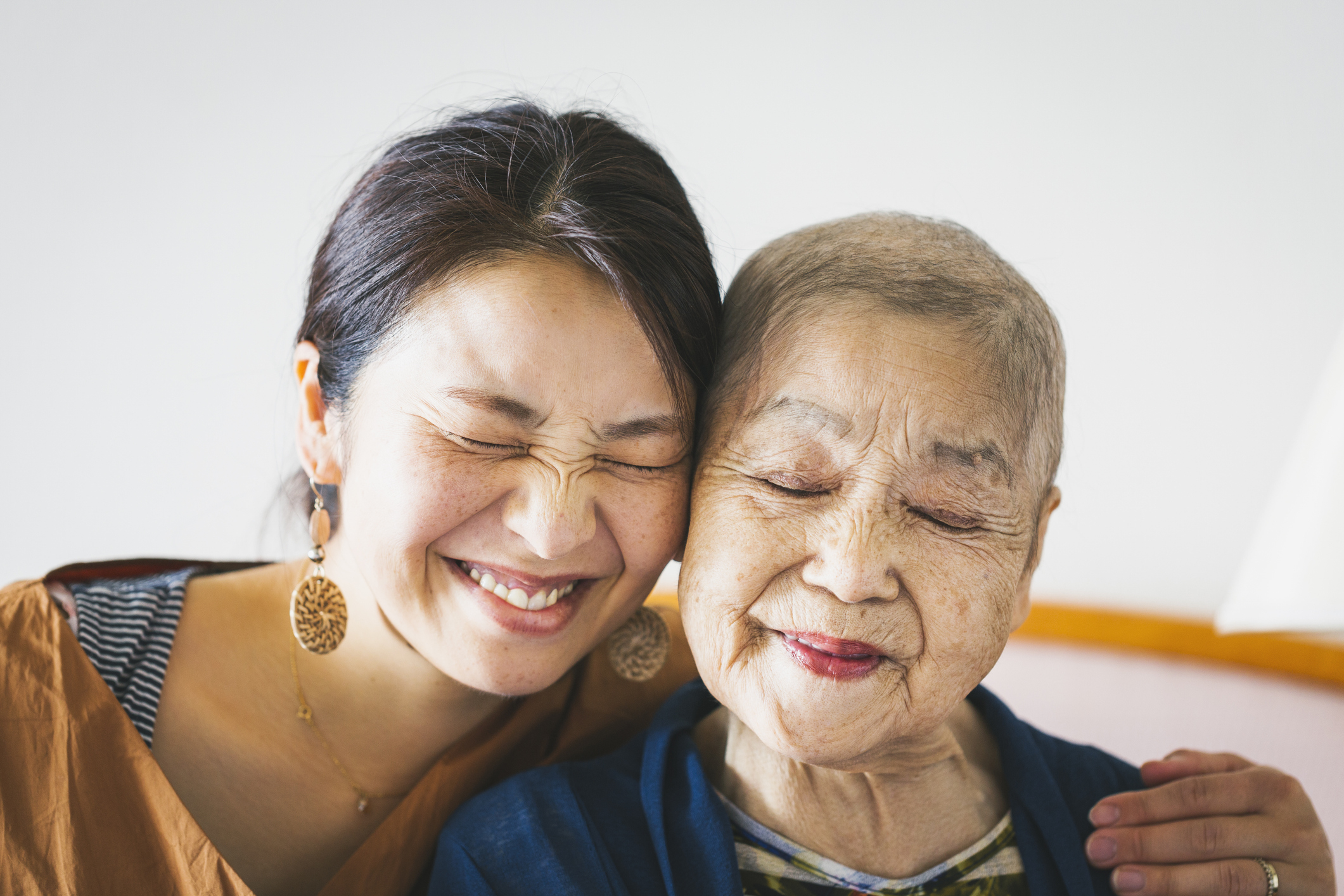 Two women embrace and smile warmly, eyes closed, radiating happiness and affection