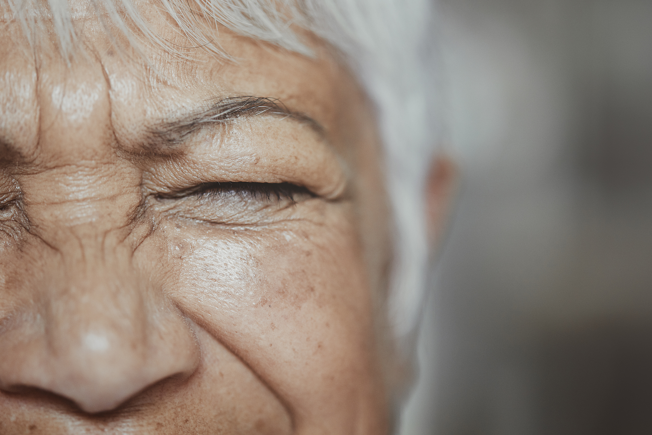 Close-up of an elderly person&#x27;s face with eyes tightly shut, highlighting wrinkles and skin texture