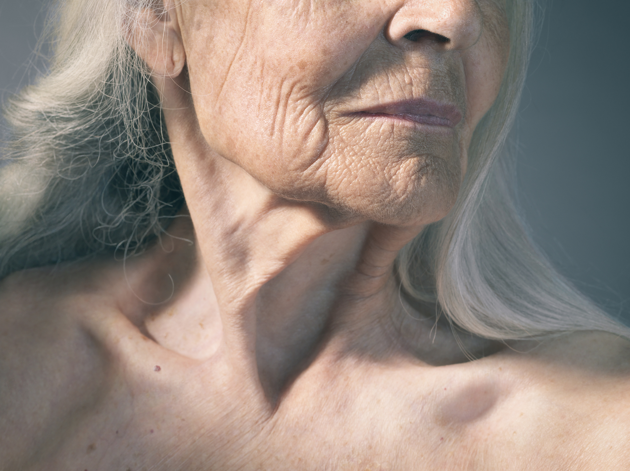Close-up of an elderly person&#x27;s face and neck showing detailed skin texture and wrinkles, indicating aging. The person is looking slightly to the side