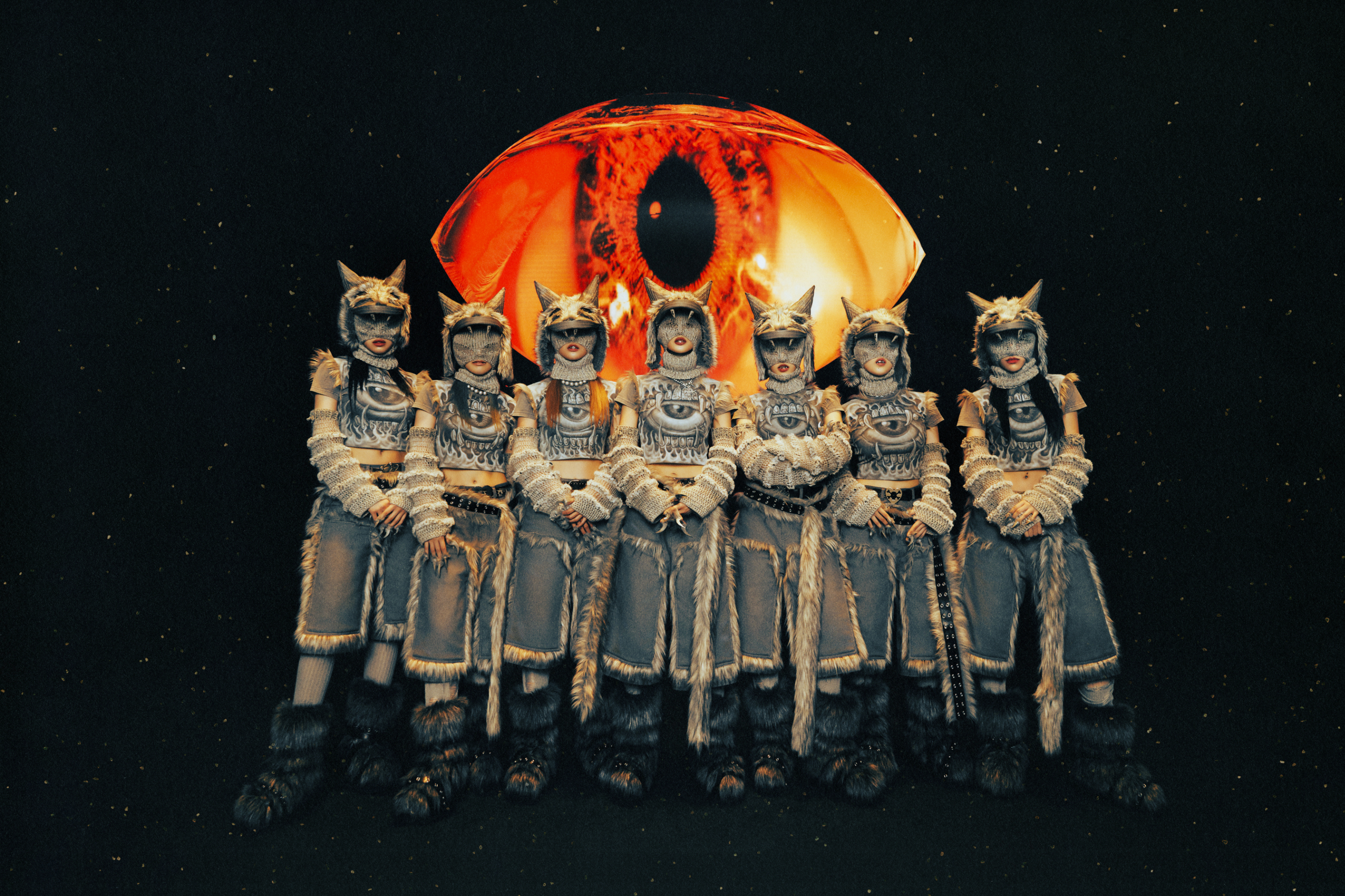 Seven people dressed in animal-themed costumes pose in front of an eye-shaped backdrop