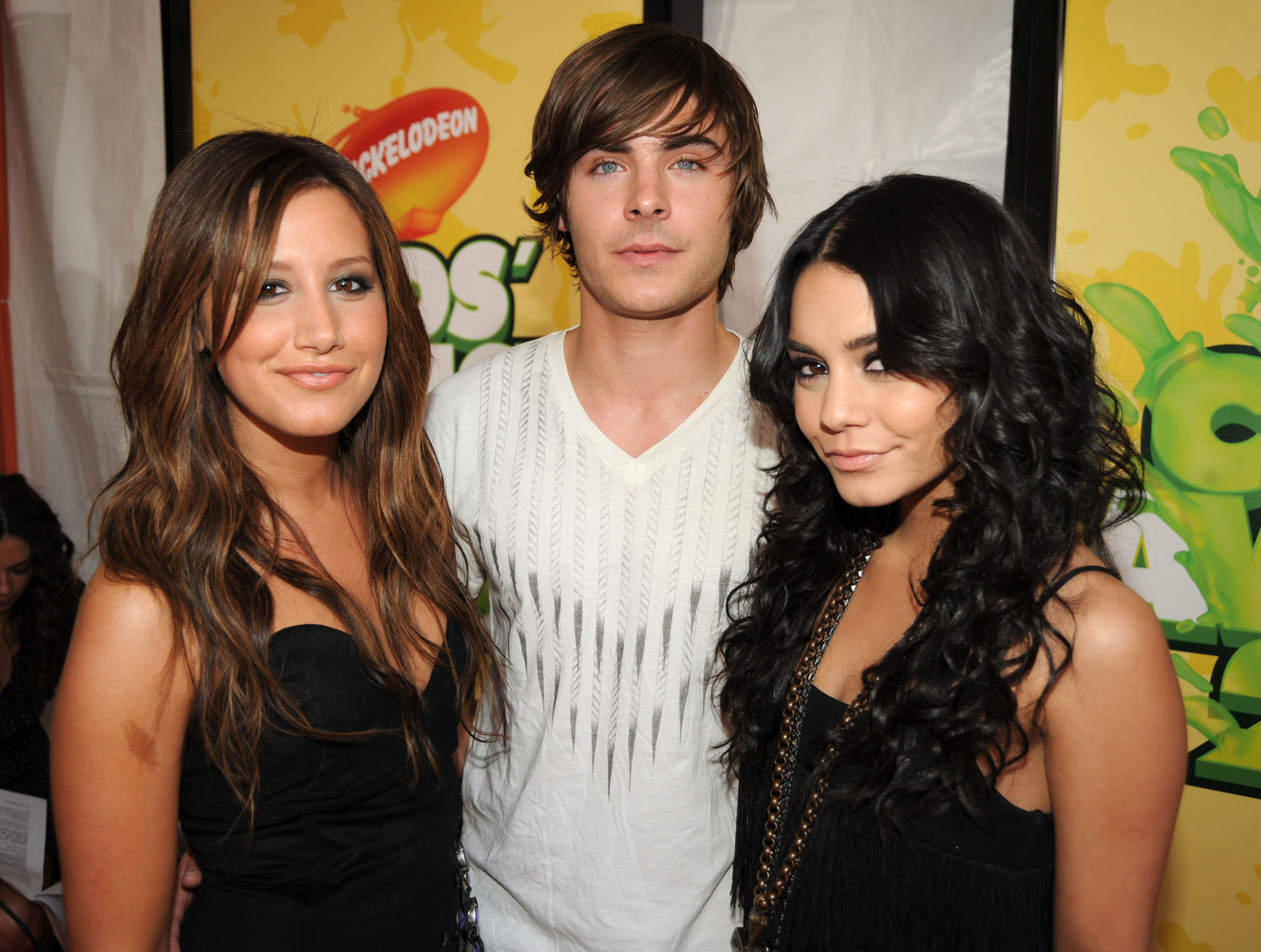 Ashley Tisdale, Zac Efron, and Vanessa Hudgens pose together at a Nickelodeon event. Tisdale wears a strapless dress, Efron in a patterned shirt, Hudgens in a chain strap dress