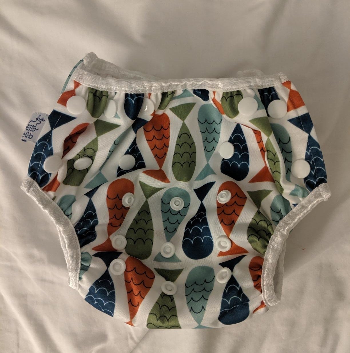 Reviewer&#x27;s photo of the reusable swim diaper with a multicolored fish pattern, laid flat on a white surface