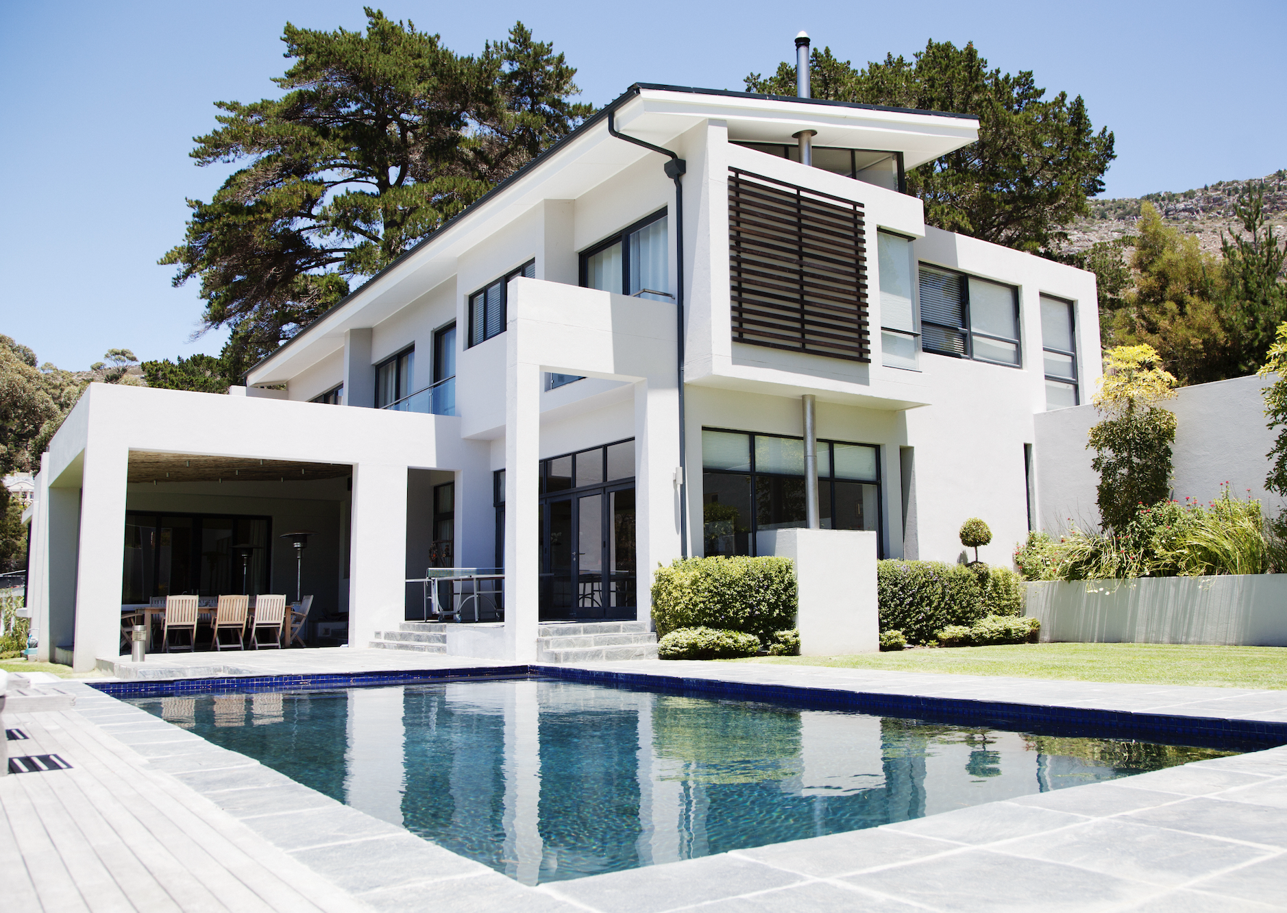 Modern two-story house with a swimming pool, large windows, patio, and surrounding greenery