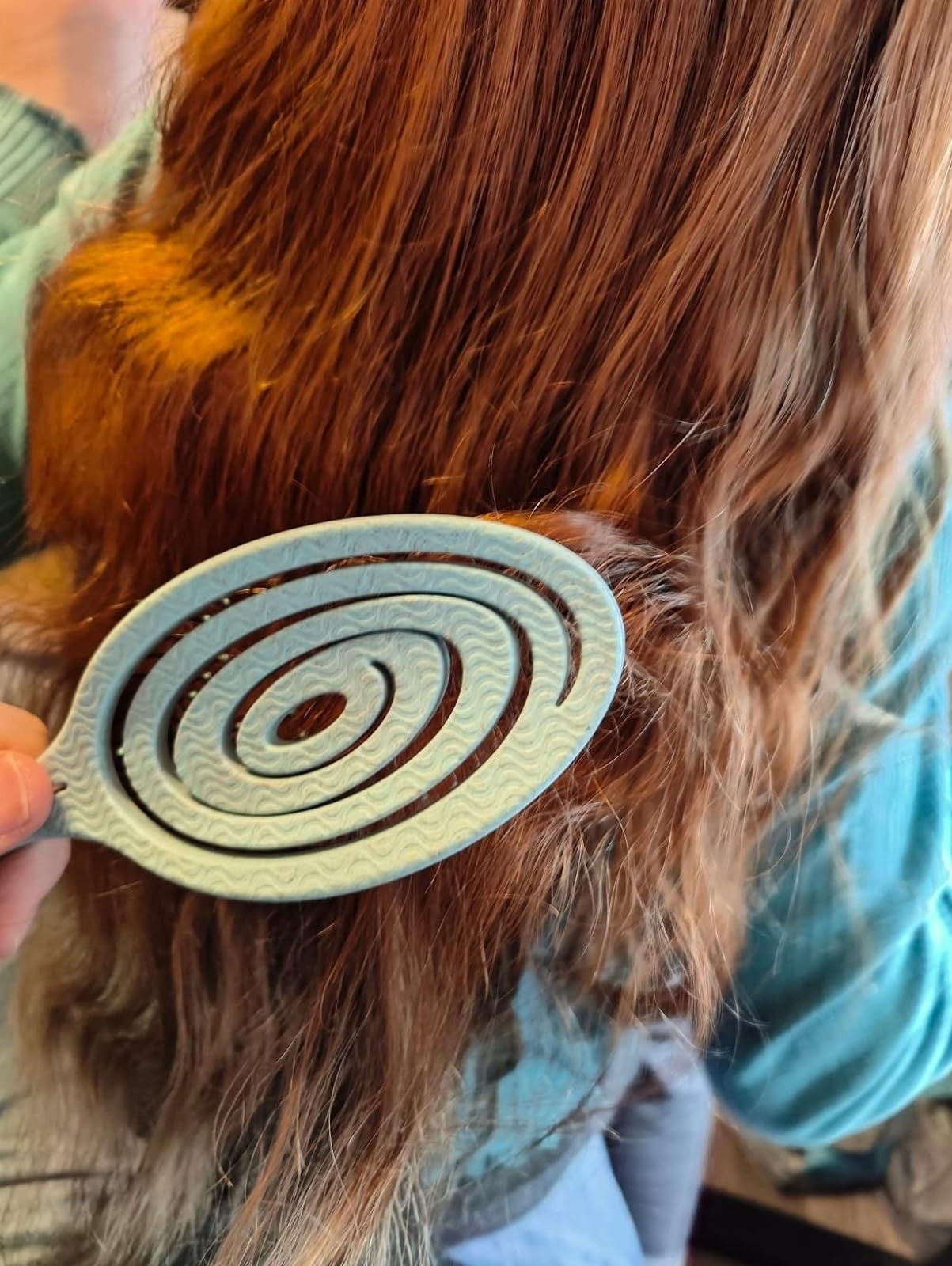 A person using a spiral detangler to brush through long hair