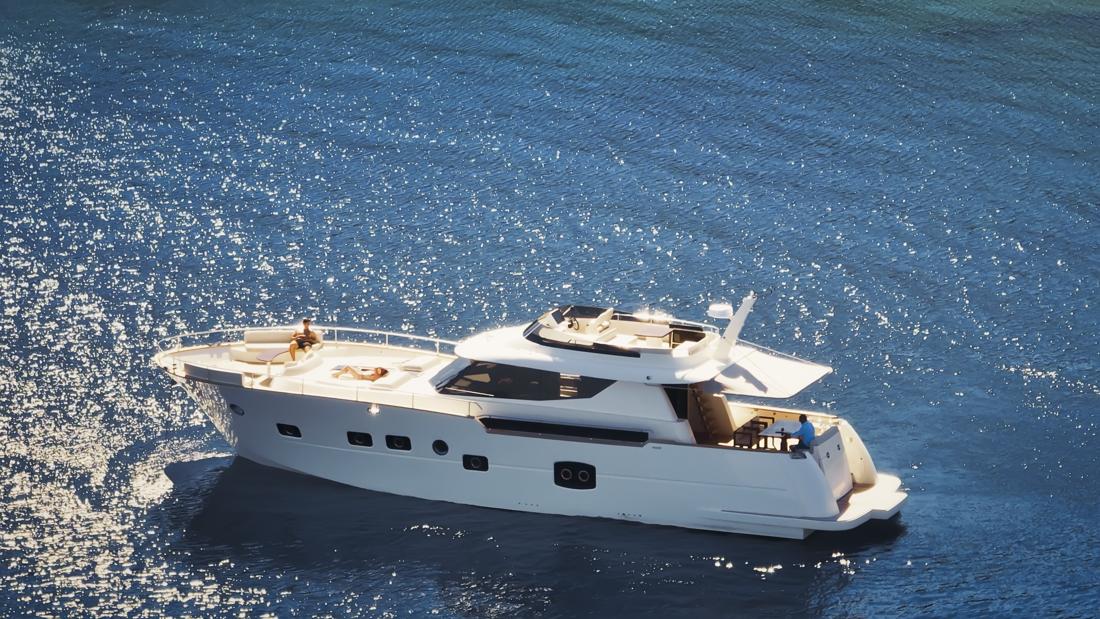 Aerial view of a white yacht cruising on clear blue ocean water with sparkling reflections from the sun