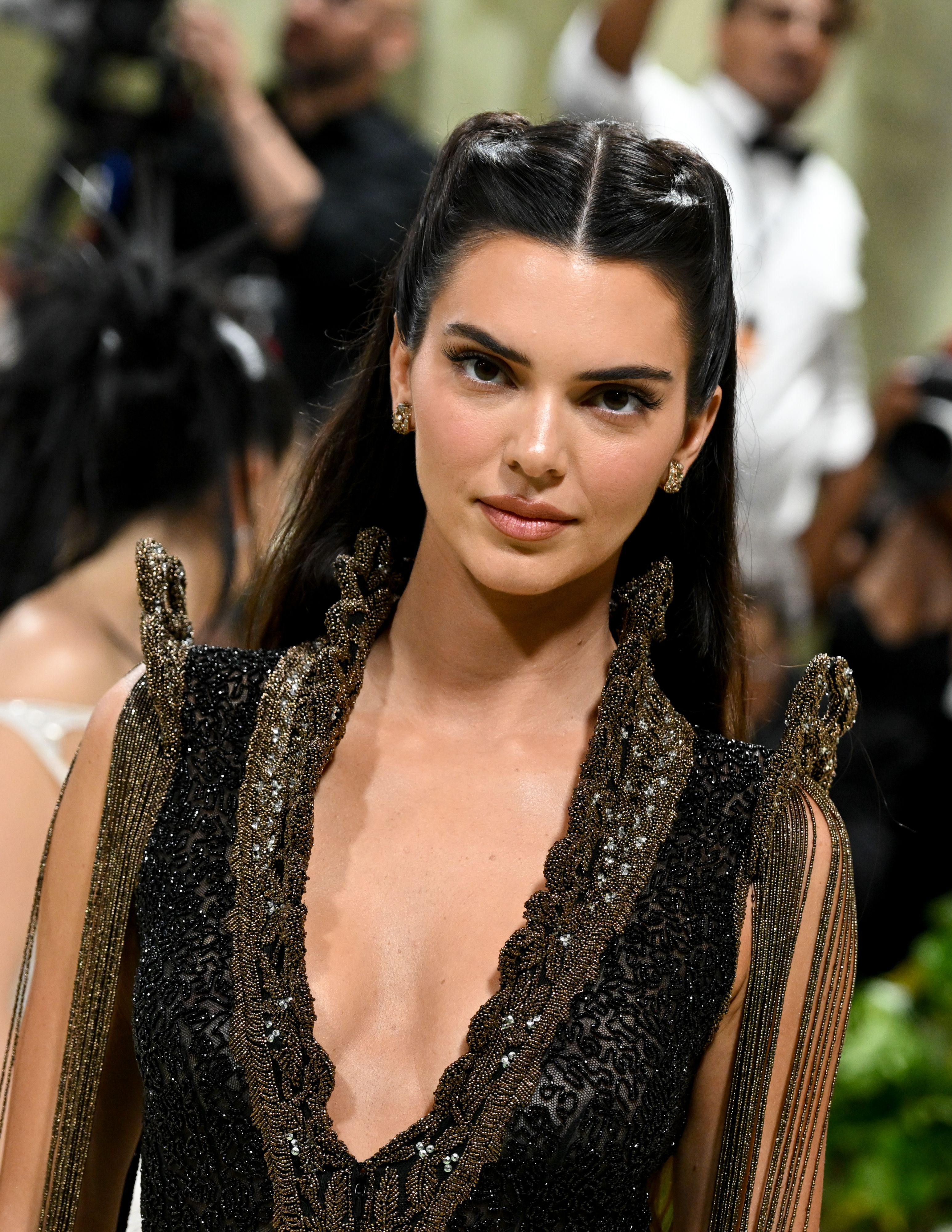 Kendall Jenner at an event, wearing an ornate, deep V-neck dress with intricate embellishments