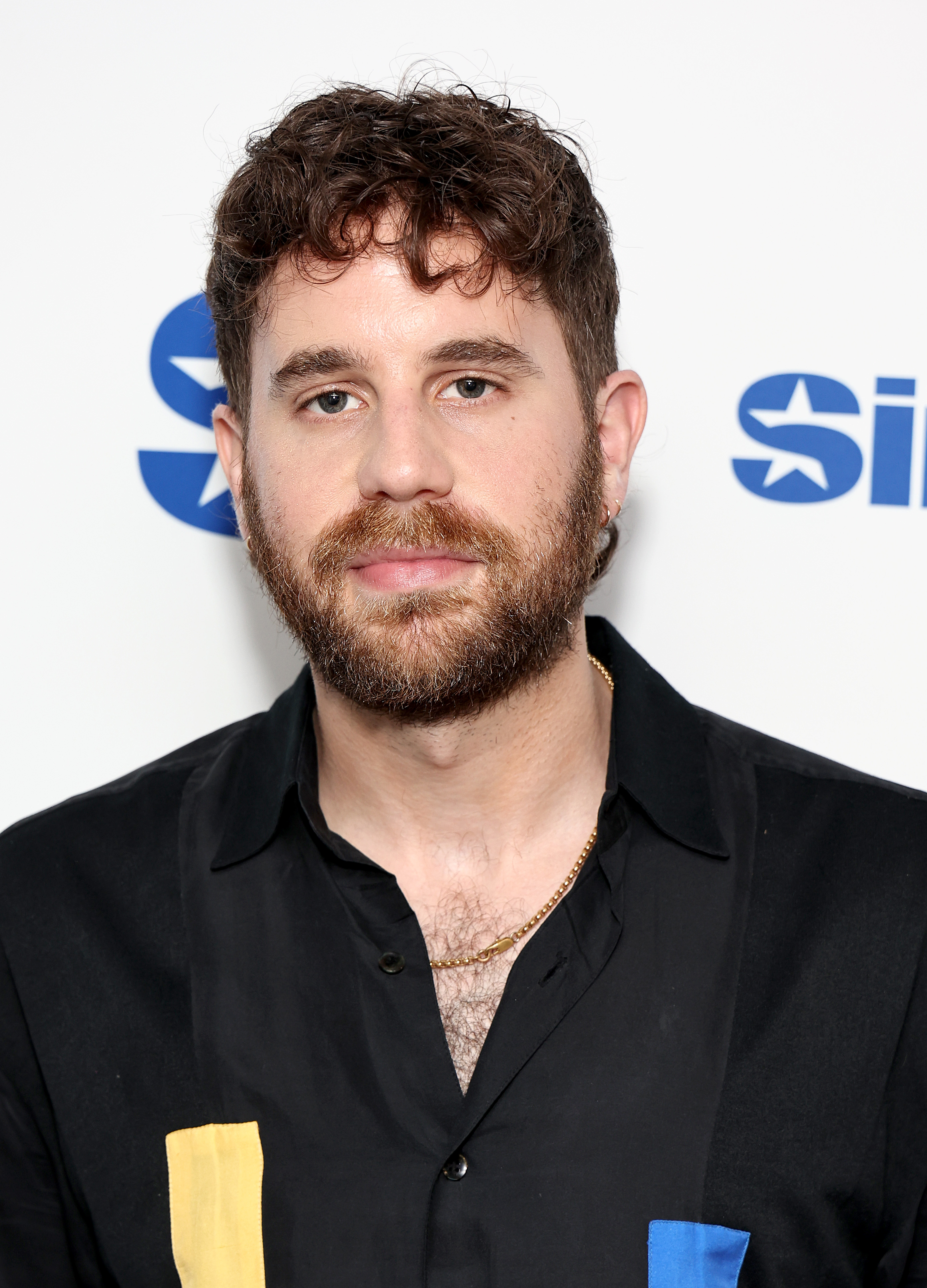 Ben Platt at an event, wearing a black shirt with color block details and a gold chain necklace