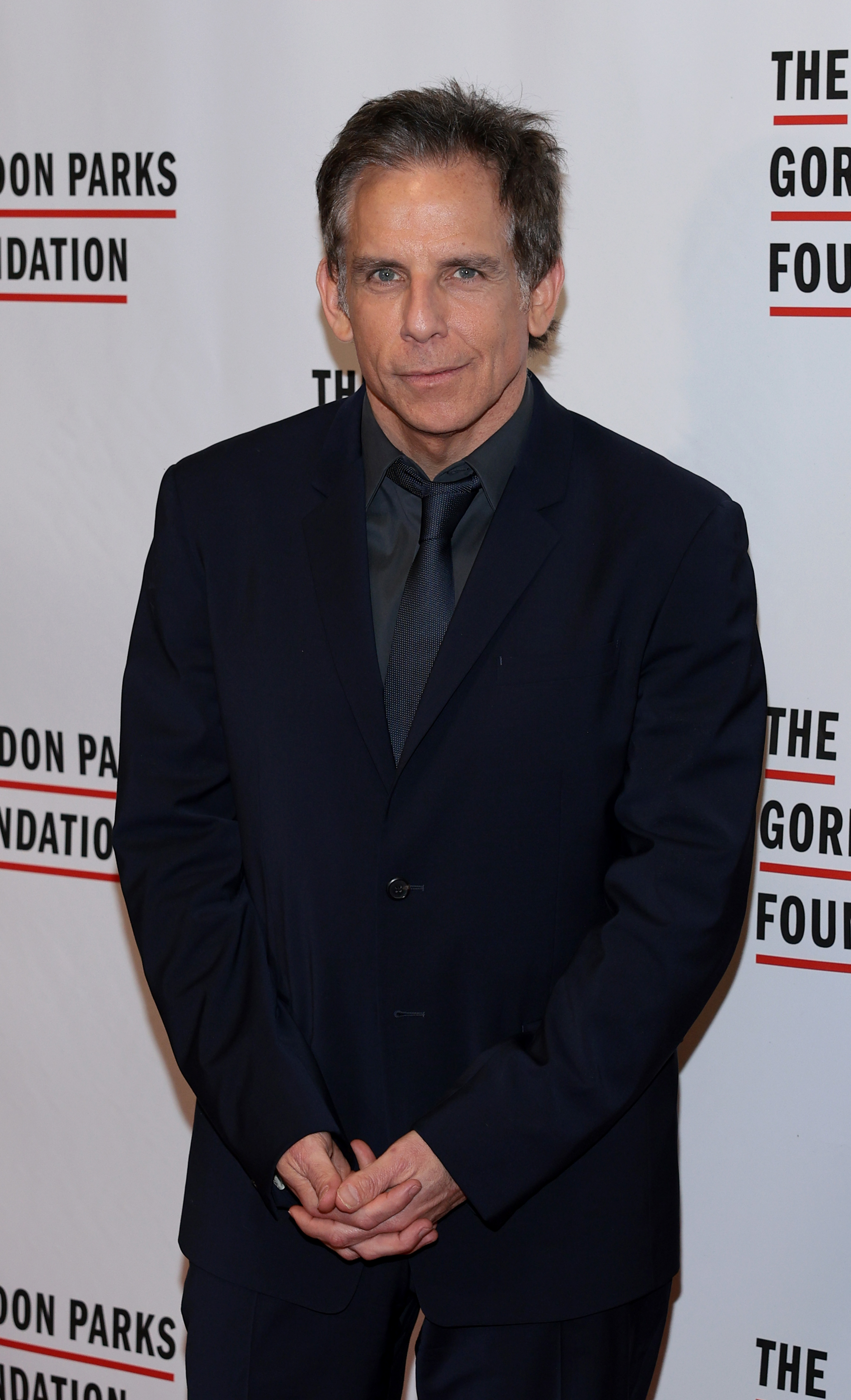 Ben Stiller at The Gordon Parks Foundation event, dressed in a dark suit and tie, posing in front of a step-and-repeat banner