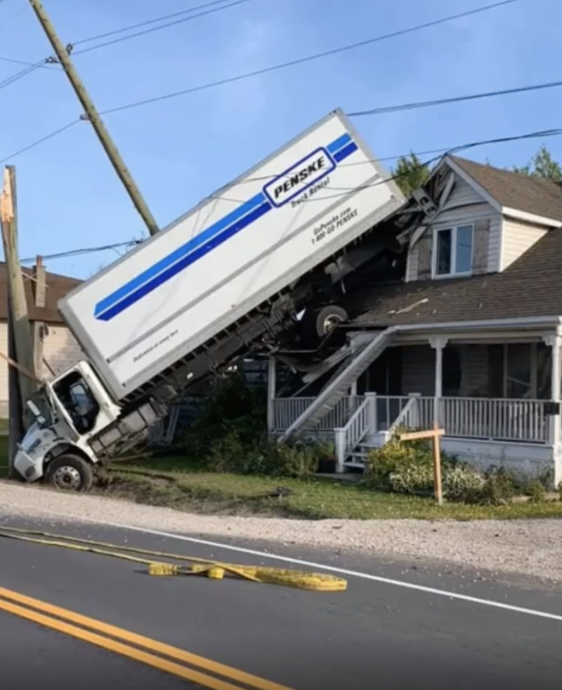 A Penske moving truck is lifted off the ground, crashed into the side of a house, causing structural damage. Power lines are down nearby