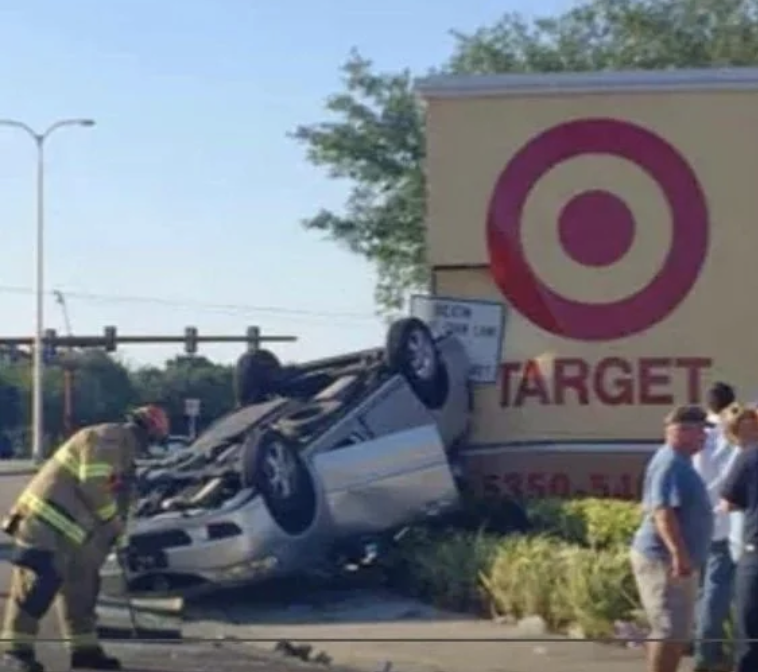 A flipped car is seen in front of a Target store with a firefighter examining the scene and several bystanders looking on