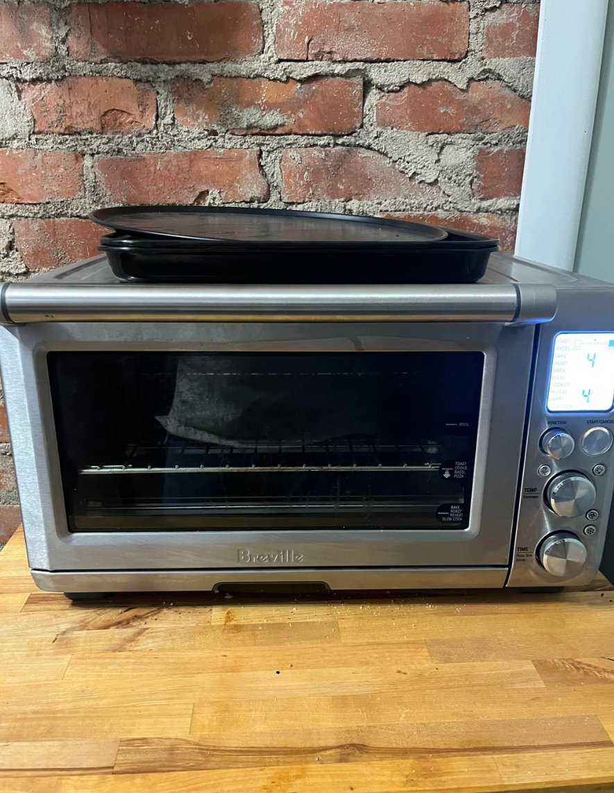 Countertop Breville toaster oven with a black tray on top, set against a brick wall background