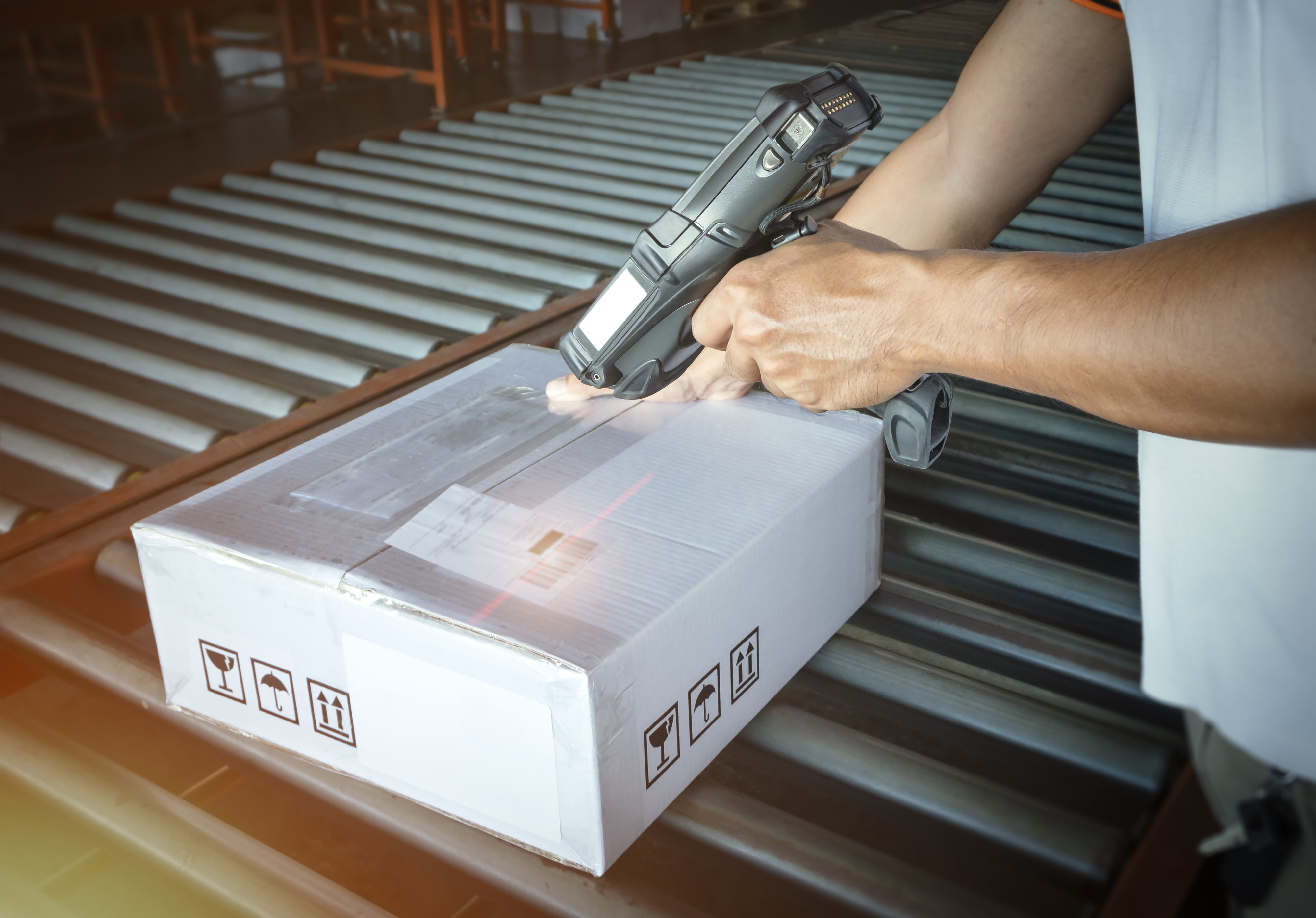 A person is scanning a package with a handheld barcode scanner in a warehouse setting