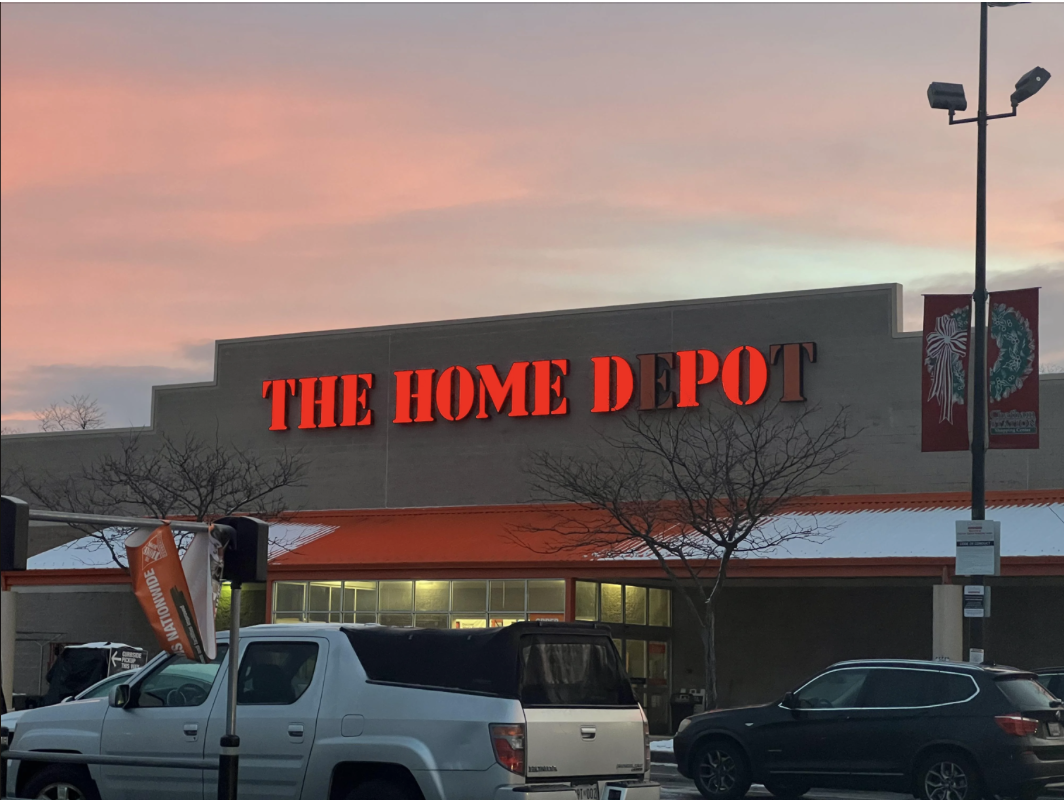 The exterior of a Home Depot store at sunset with cars parked in the foreground