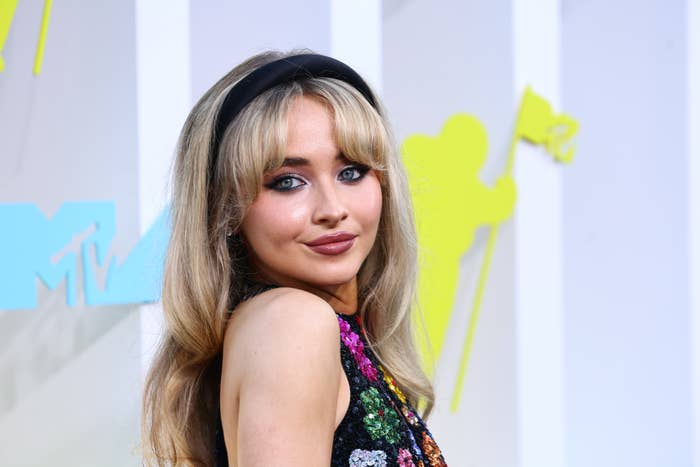 Sabrina Carpenter on the MTV Awards red carpet, wearing a sleeveless sequined dress and a headband, smiling at the camera
