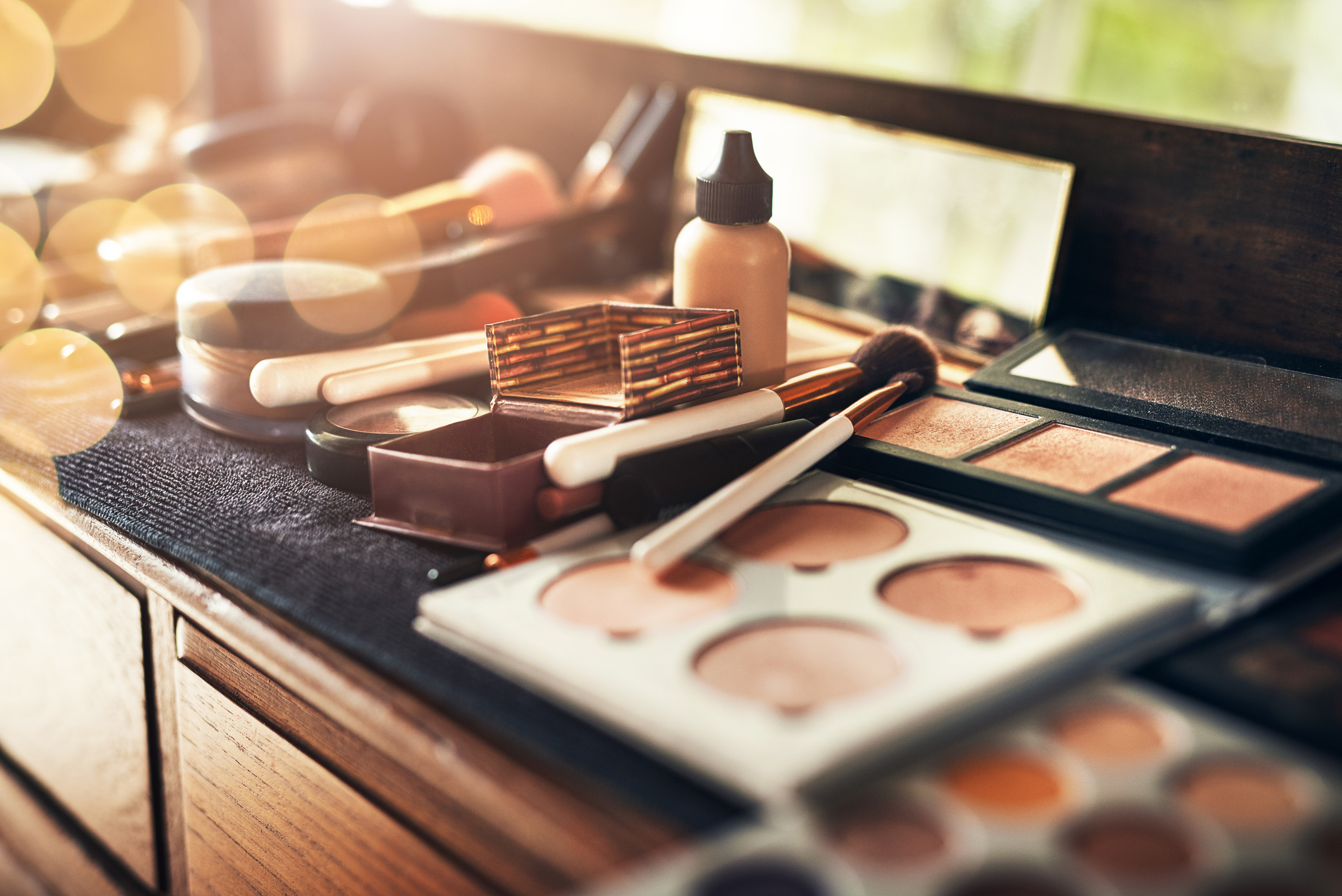 A vanity table featuring various makeup items including brushes, foundation, and palettes, with a mirror in the background