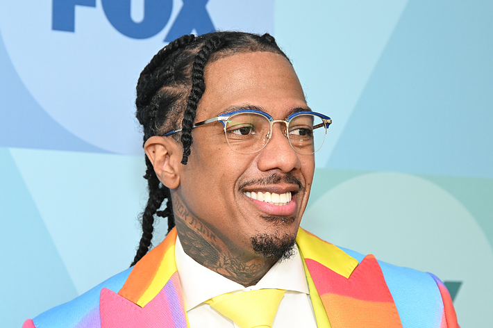 Nick Cannon wearing a vibrant, multi-colored suit with a yellow tie poses on the FOX blue-carpet event backdrop