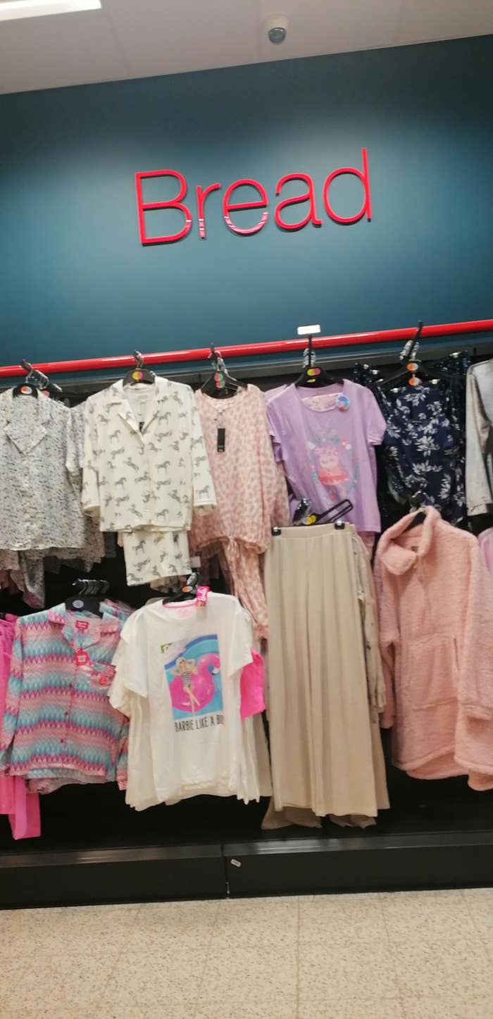 A store section labeled &quot;Bread&quot; with various clothes, including shirts and dresses, hanging underneath the sign